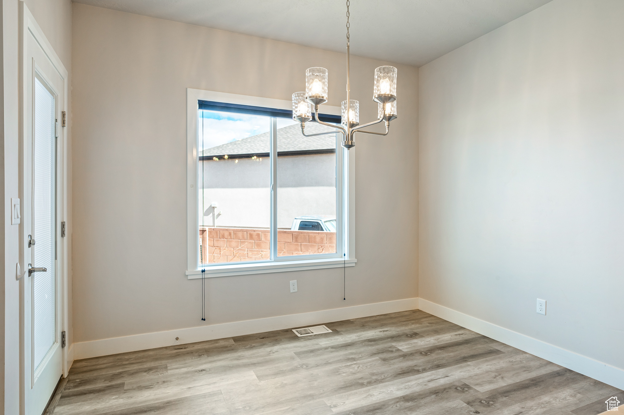 Unfurnished dining area featuring an inviting chandelier, a healthy amount of sunlight, and light hardwood / wood-style flooring