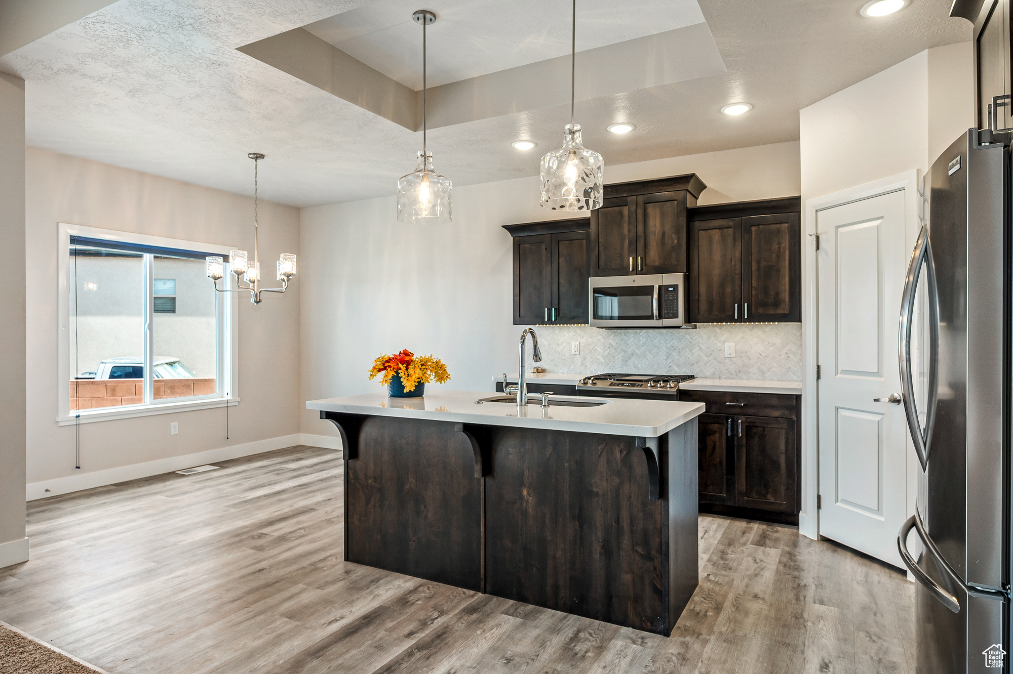 Kitchen featuring appliances with stainless steel finishes, sink, hanging light fixtures, dark brown cabinets, and a kitchen island with sink