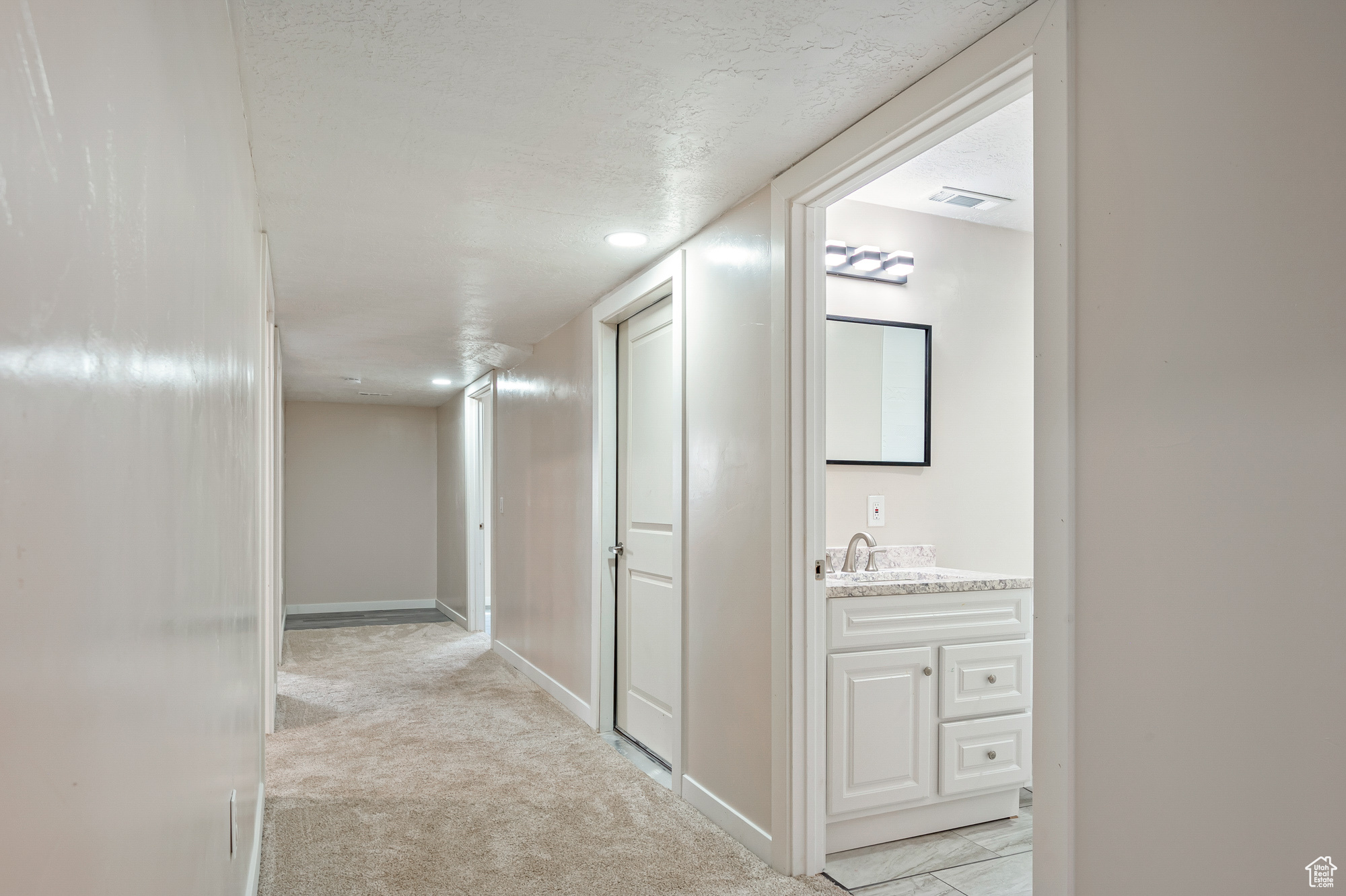 Hallway featuring a textured ceiling, sink, and light colored carpet