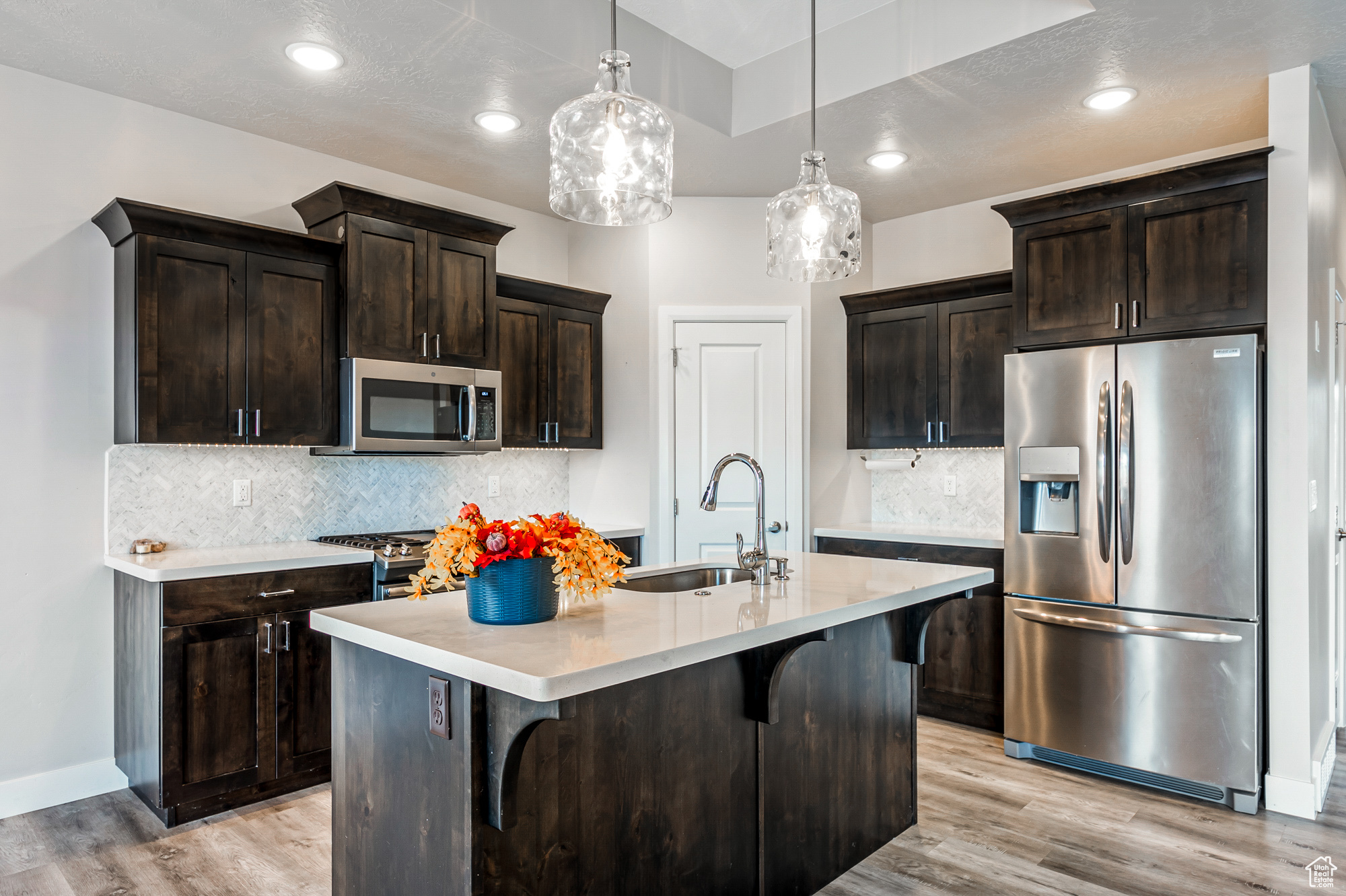 Kitchen featuring a center island with sink, a breakfast bar, dark brown cabinetry, decorative light fixtures, and appliances with stainless steel finishes