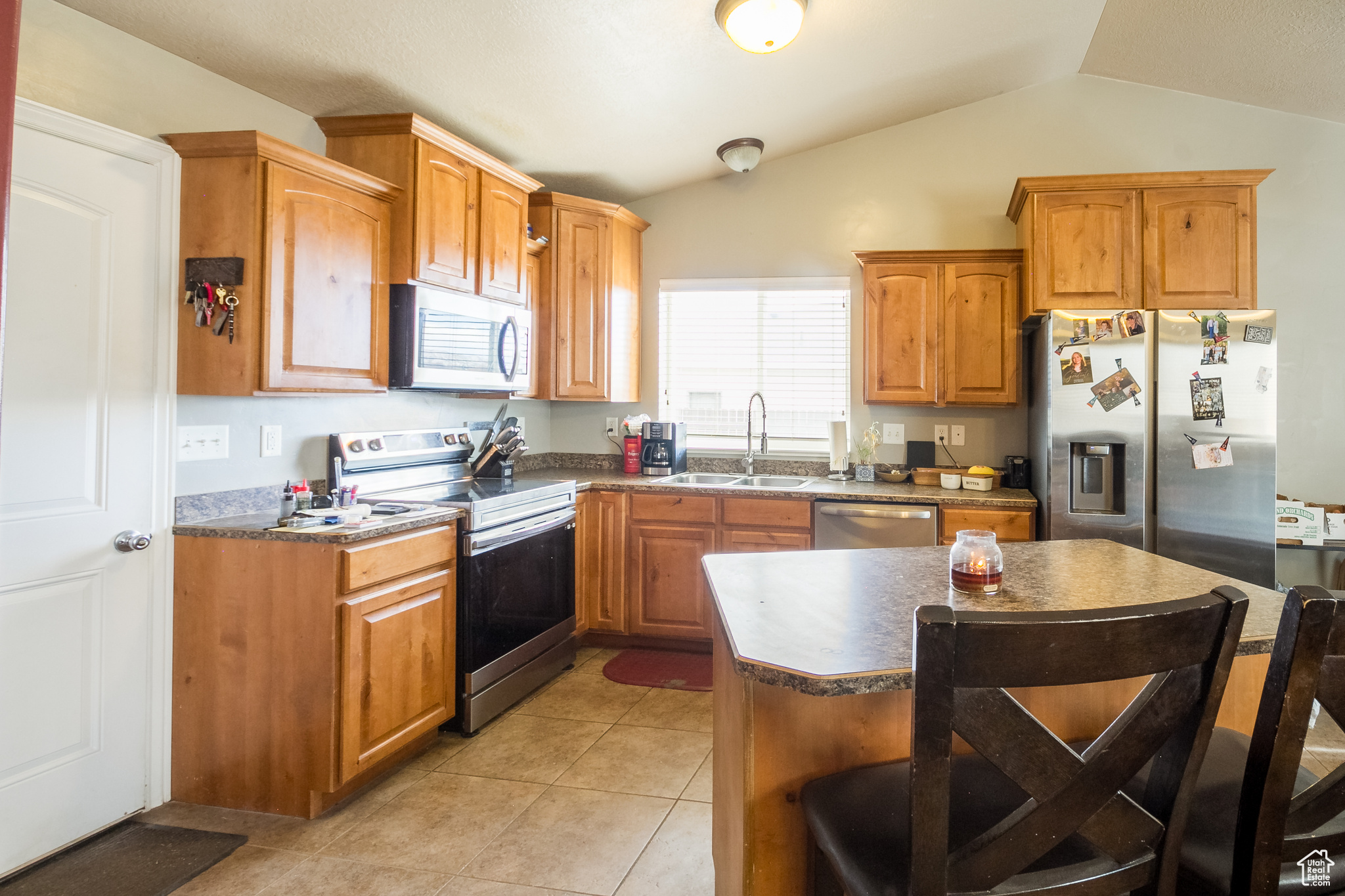 Kitchen with appliances with stainless steel finishes, light tile patterned floors, sink, and lofted ceiling