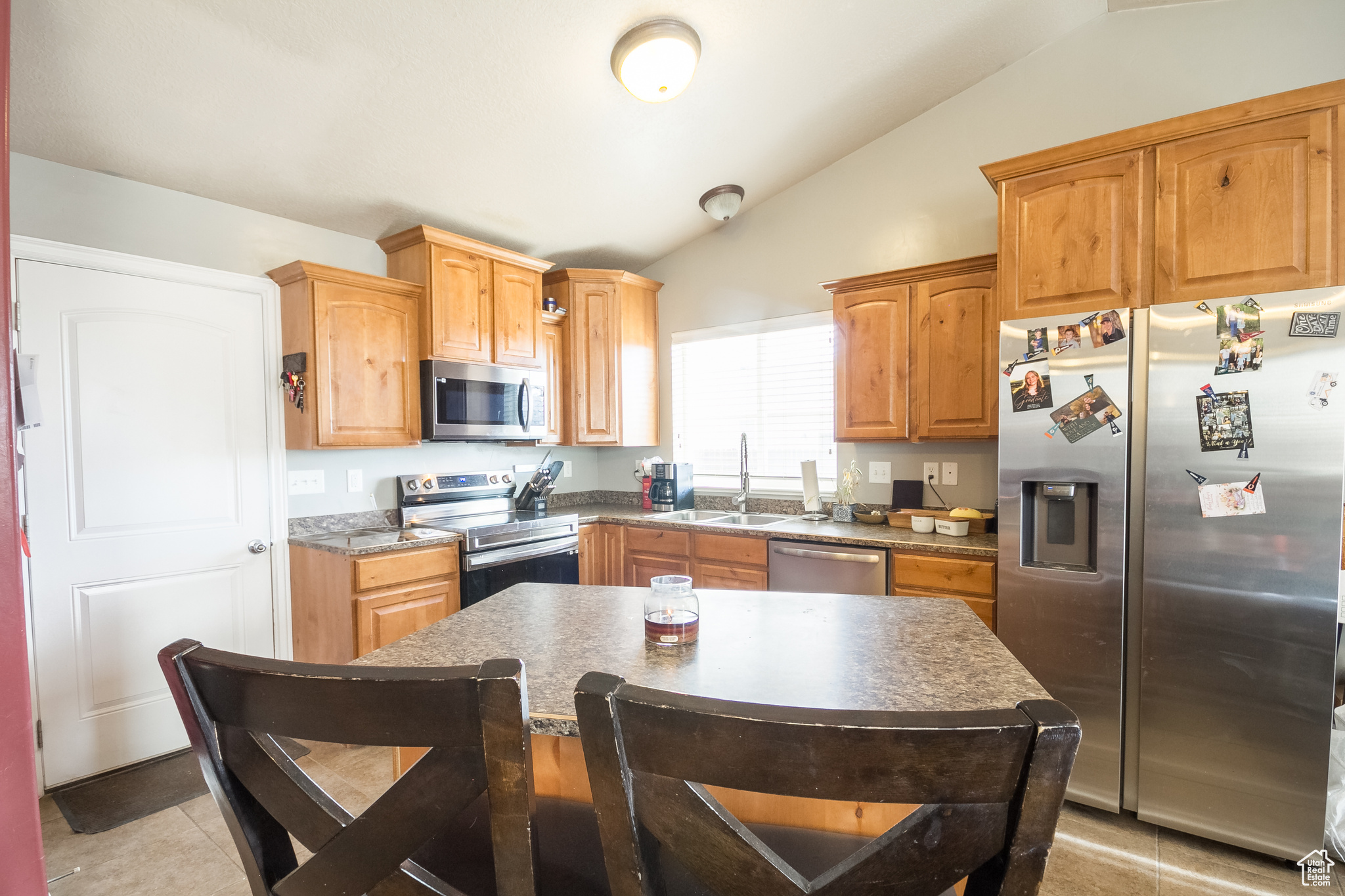 Kitchen with stainless steel appliances, lofted ceiling, light tile patterned flooring, a kitchen island, and sink