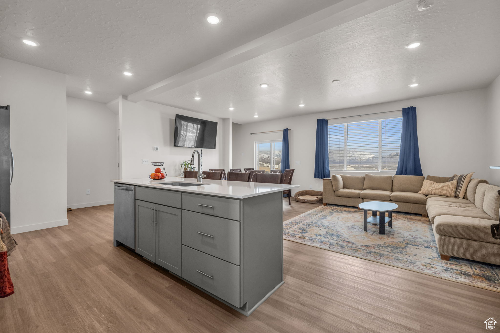 Kitchen featuring light hardwood / wood-style flooring, appliances with stainless steel finishes, gray cabinets, and a kitchen island with sink