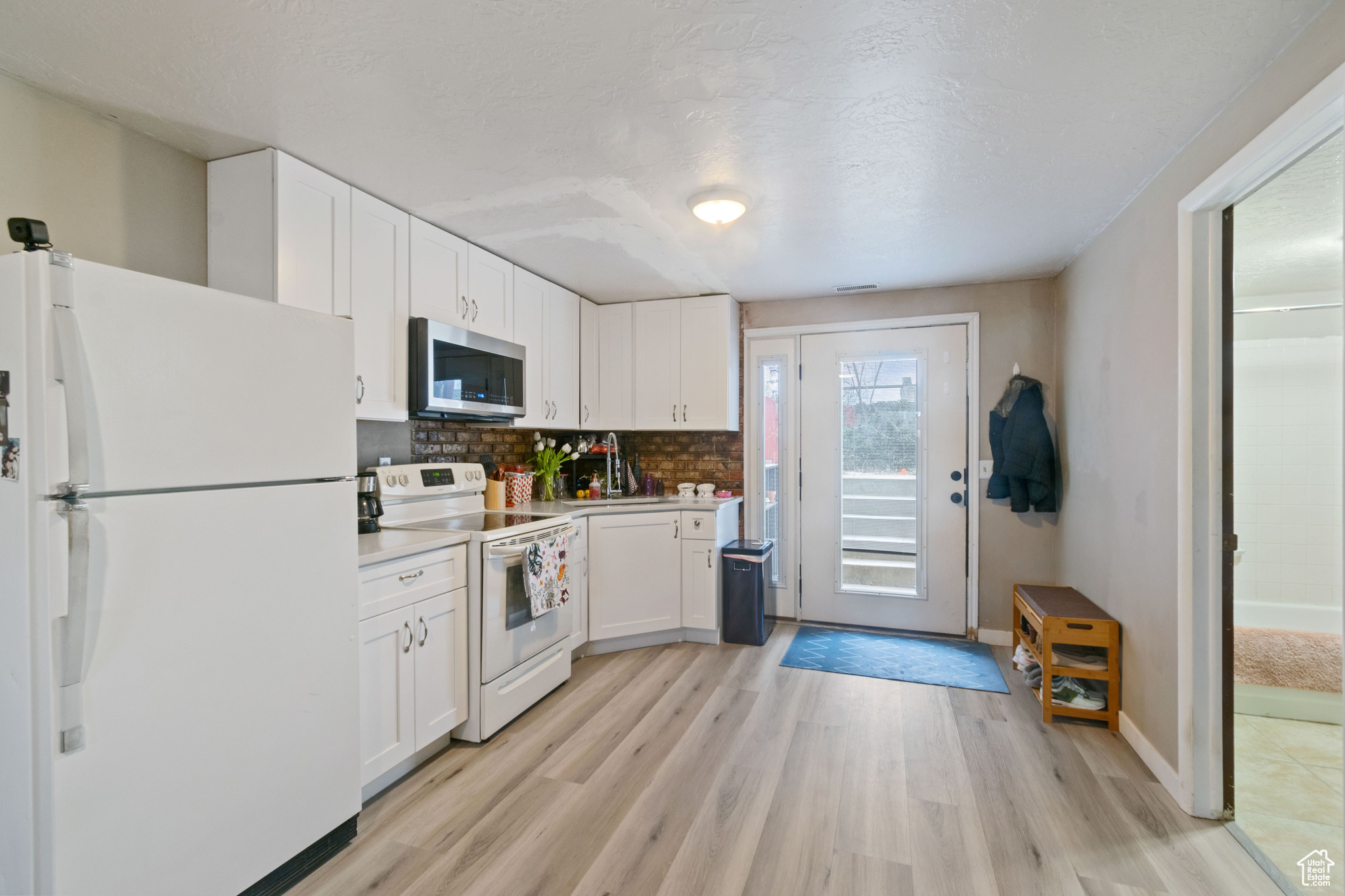 Kitchen with light countertops, light wood-type flooring, white cabinets, and white appliances