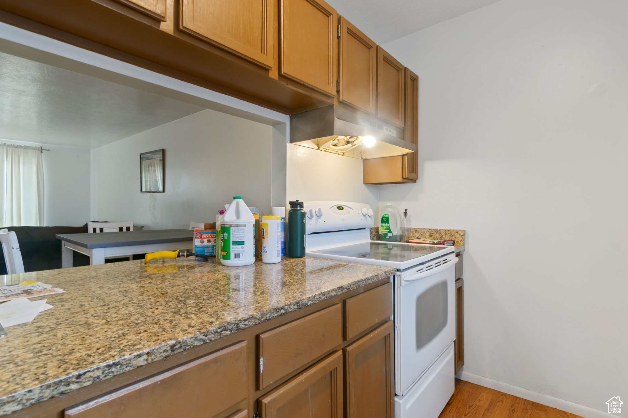 Kitchen with electric range, under cabinet range hood, light wood finished floors, baseboards, and brown cabinetry