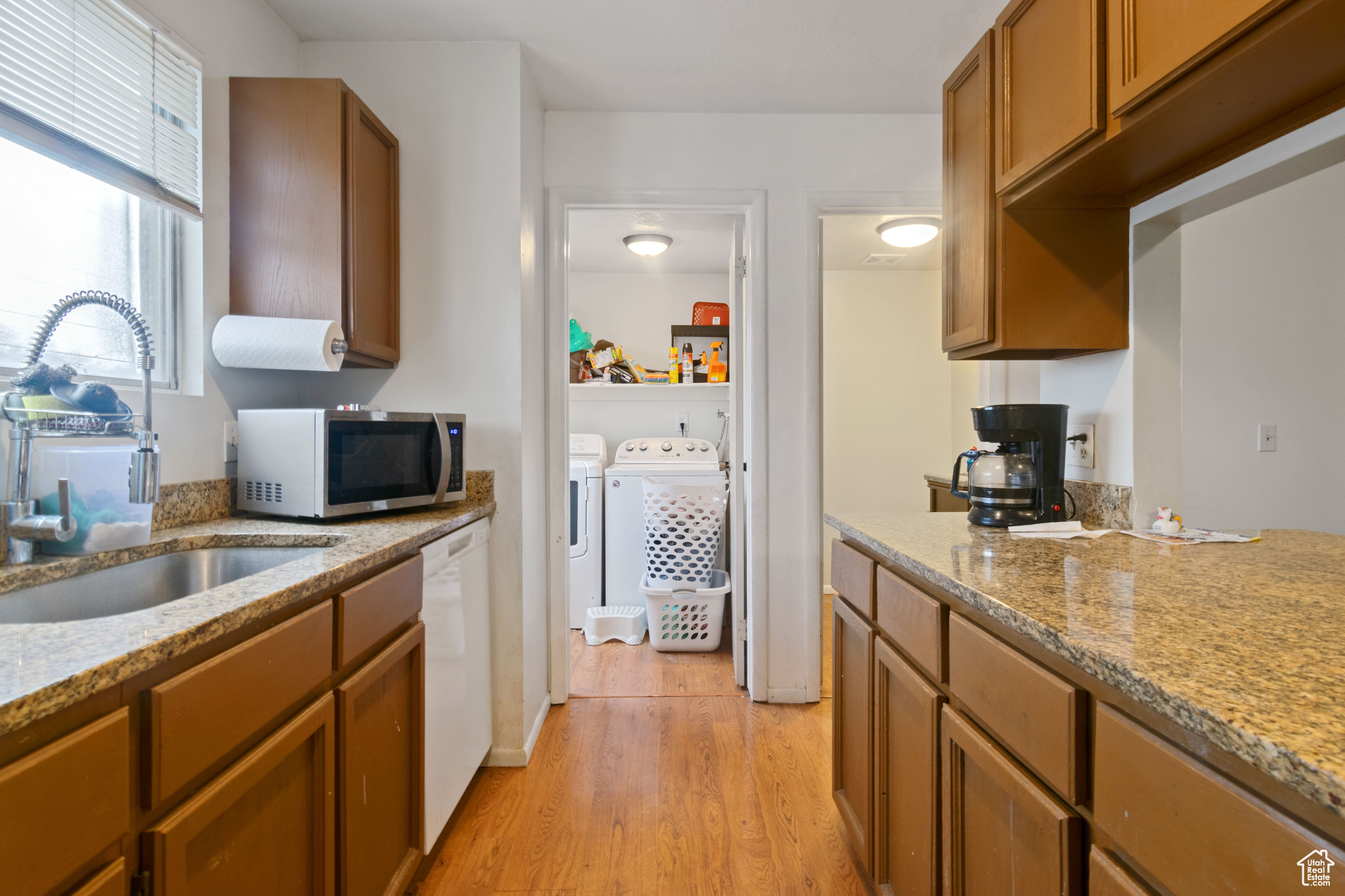 Kitchen with stainless steel microwave, a sink, washing machine and dryer, brown cabinetry, and dishwasher