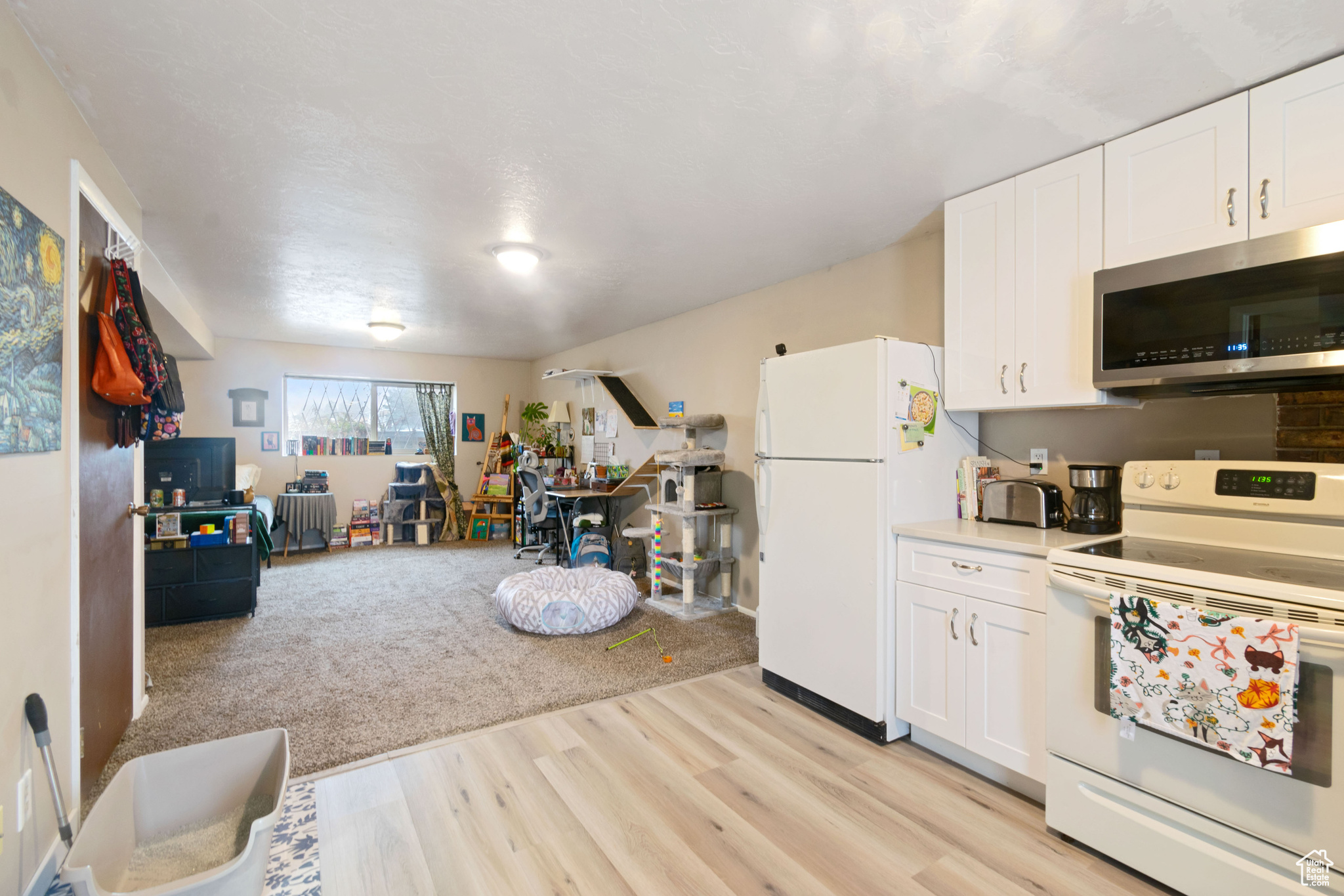 Kitchen with light countertops, white cabinets, light wood-style flooring, and white appliances