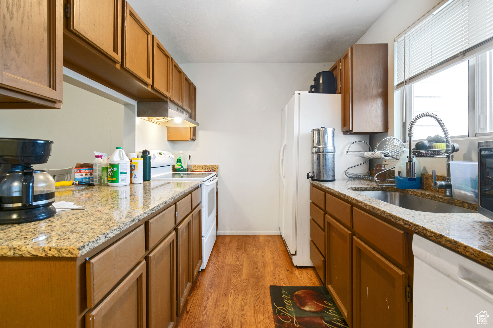 Kitchen featuring a sink, brown cabinets, white appliances, and under cabinet range hood
