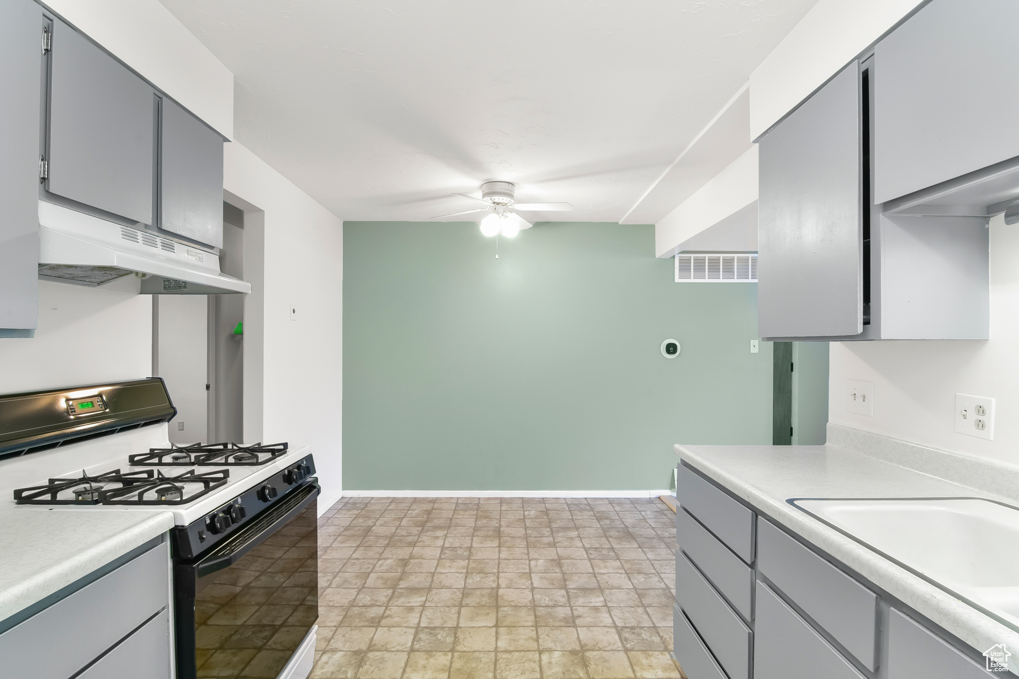 Kitchen featuring visible vents, range with gas cooktop, ceiling fan, light countertops, and under cabinet range hood