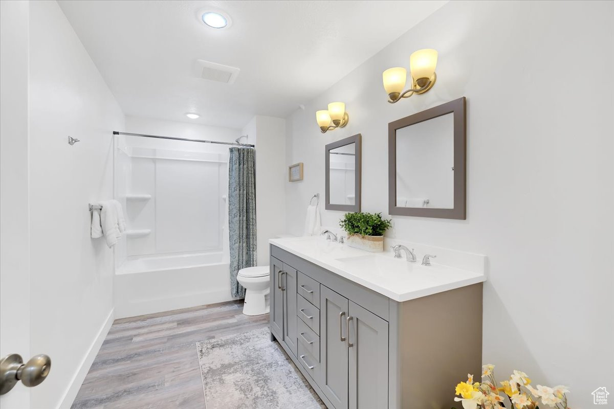 Bathroom featuring double vanity, shower / bath combo, toilet, wood finished floors, and a sink