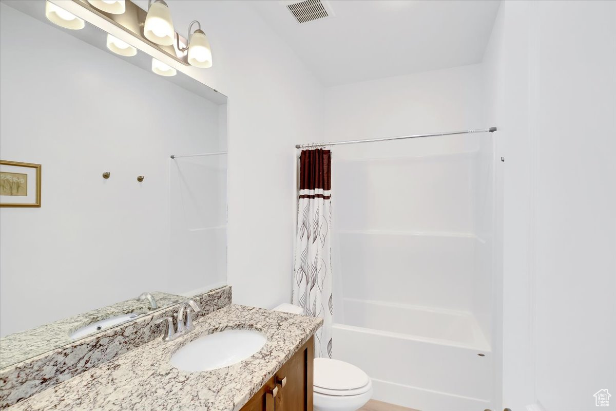 Bathroom featuring toilet, shower / tub combo, vanity, and visible vents