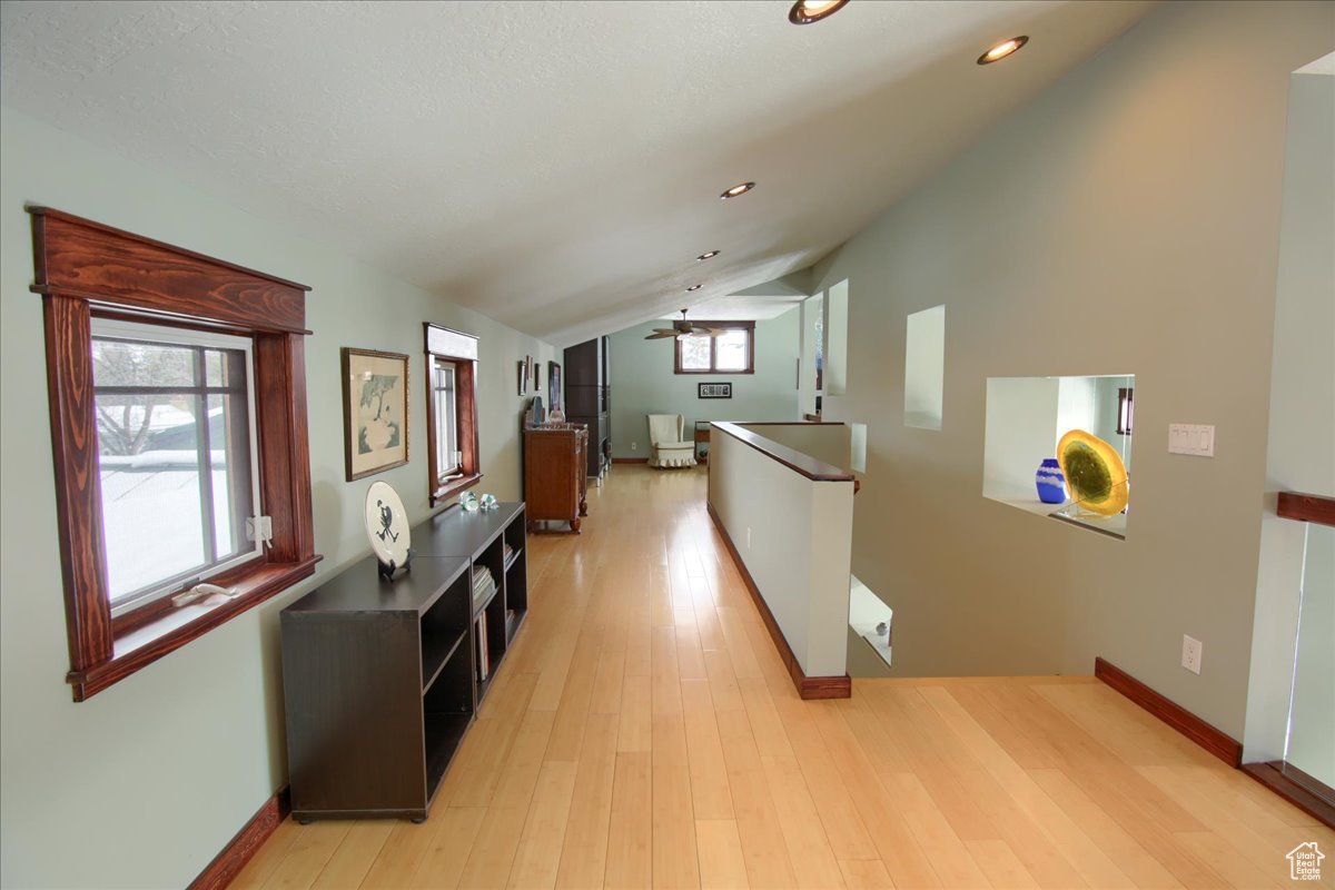 Corridor with lofted ceiling, light wood-style flooring, recessed lighting, an upstairs landing, and baseboards