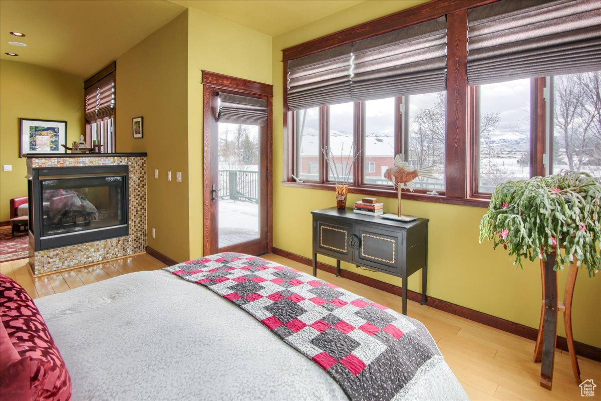 Bedroom featuring baseboards, access to exterior, light wood-type flooring, a tiled fireplace, and a wood stove