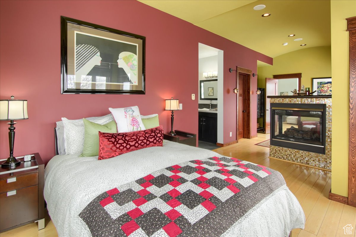 Bedroom with lofted ceiling, recessed lighting, a multi sided fireplace, baseboards, and light wood-type flooring