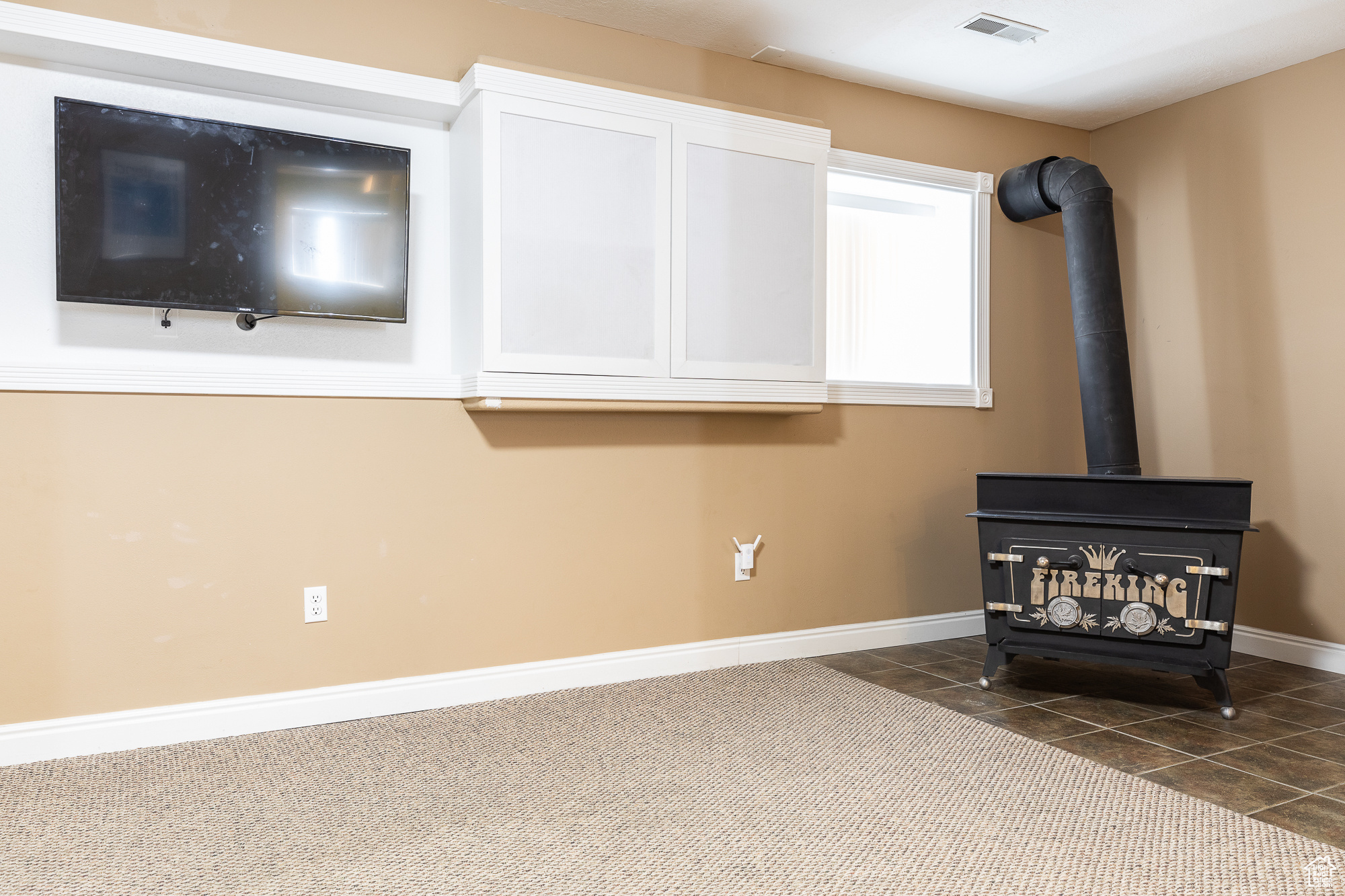 Room details featuring carpet flooring, a wood stove, visible vents, and baseboards