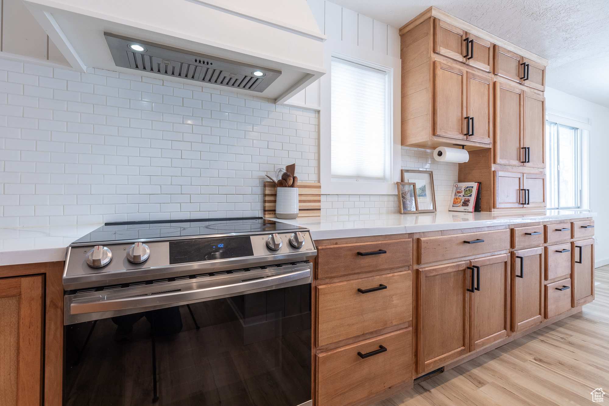 Kitchen featuring stainless steel electric stove, light wood-style floors, light countertops, custom exhaust hood, and decorative backsplash