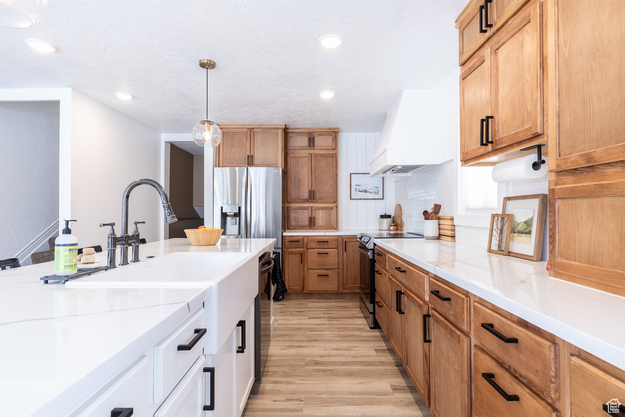 Kitchen with white cabinets, custom range hood, light stone counters, hanging light fixtures, and stainless steel appliances