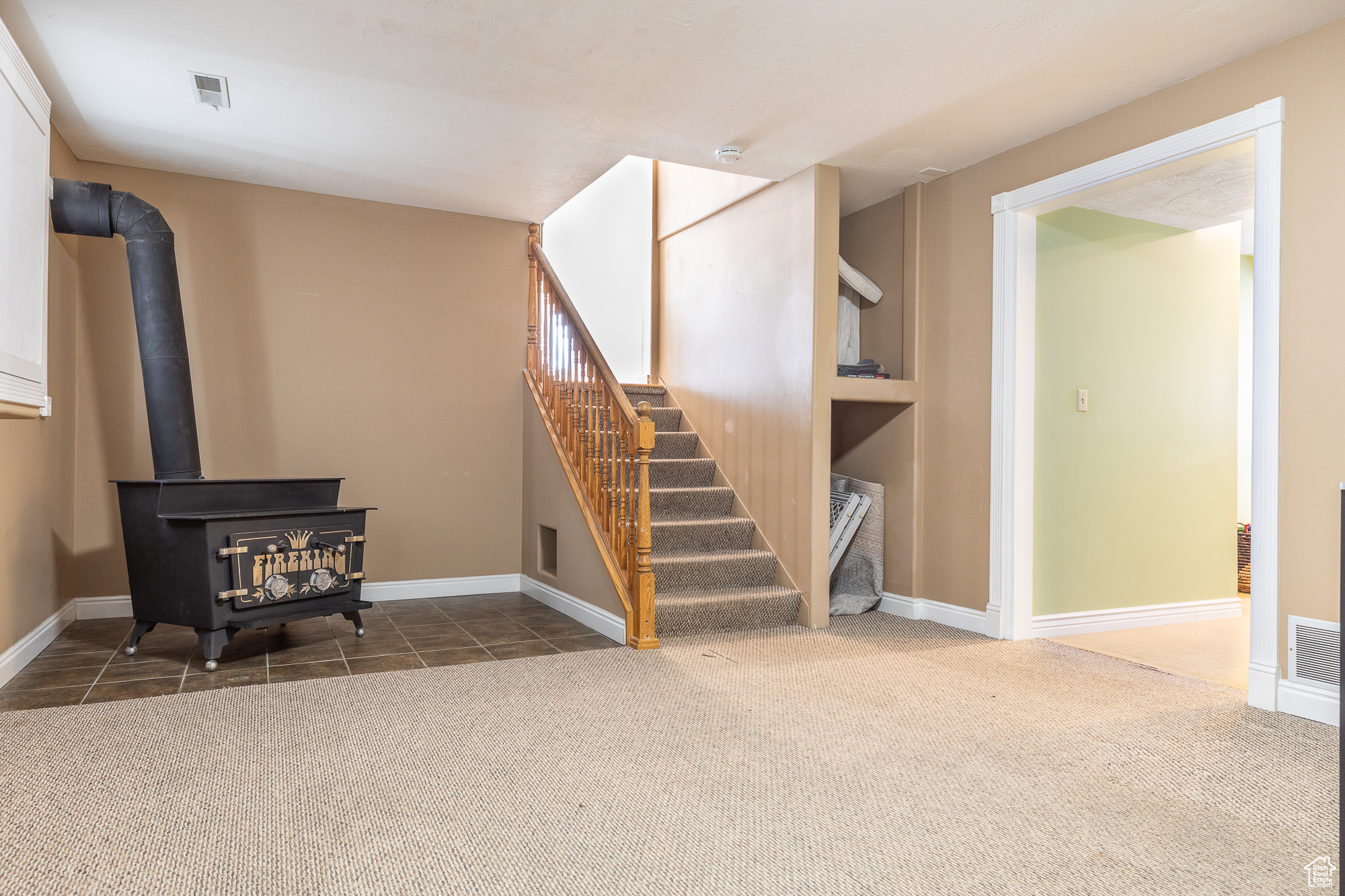 Interior space with baseboards, visible vents, stairway, a wood stove, and dark colored carpet