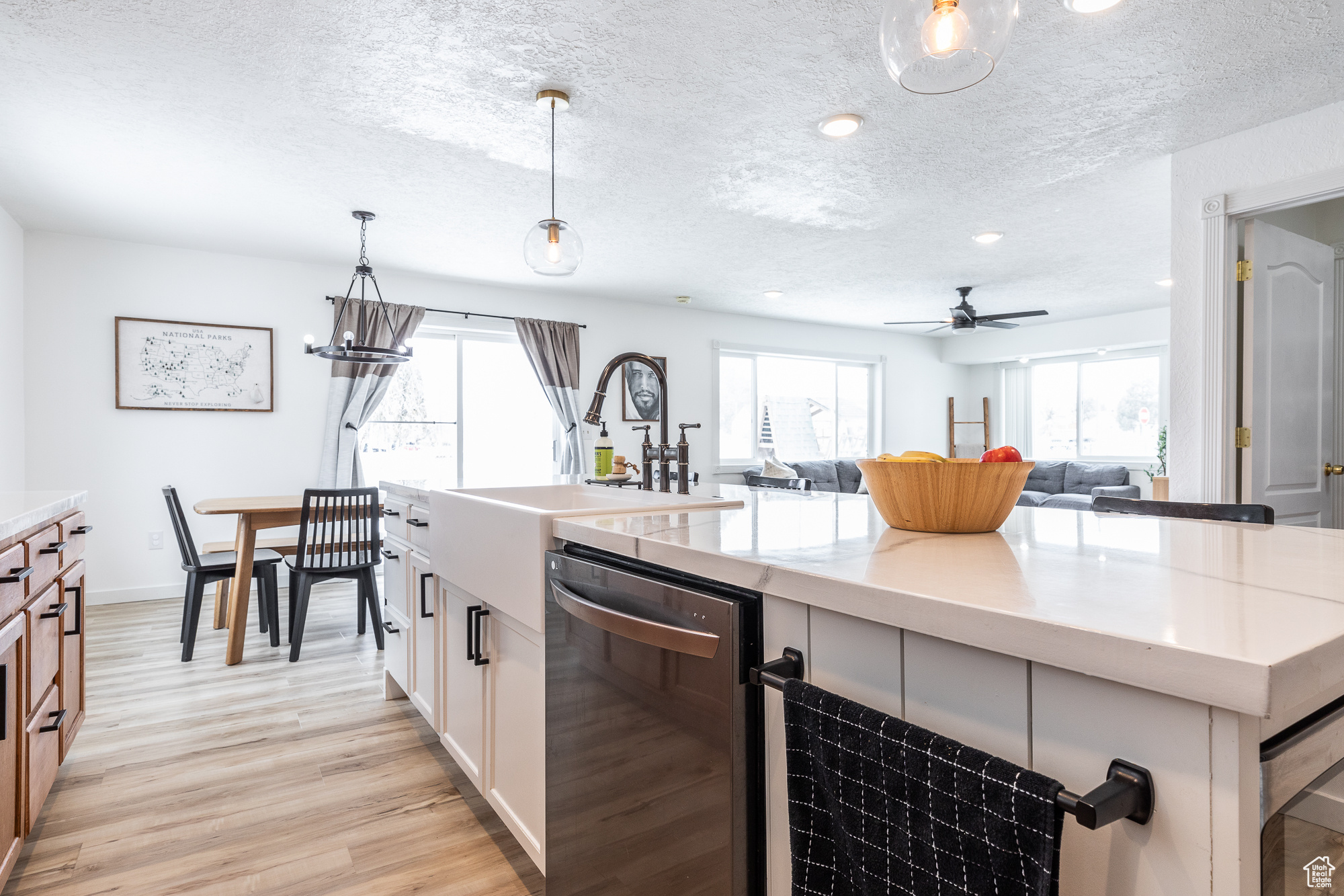 Kitchen featuring decorative light fixtures, a center island with sink, open floor plan, white cabinets, and dishwasher