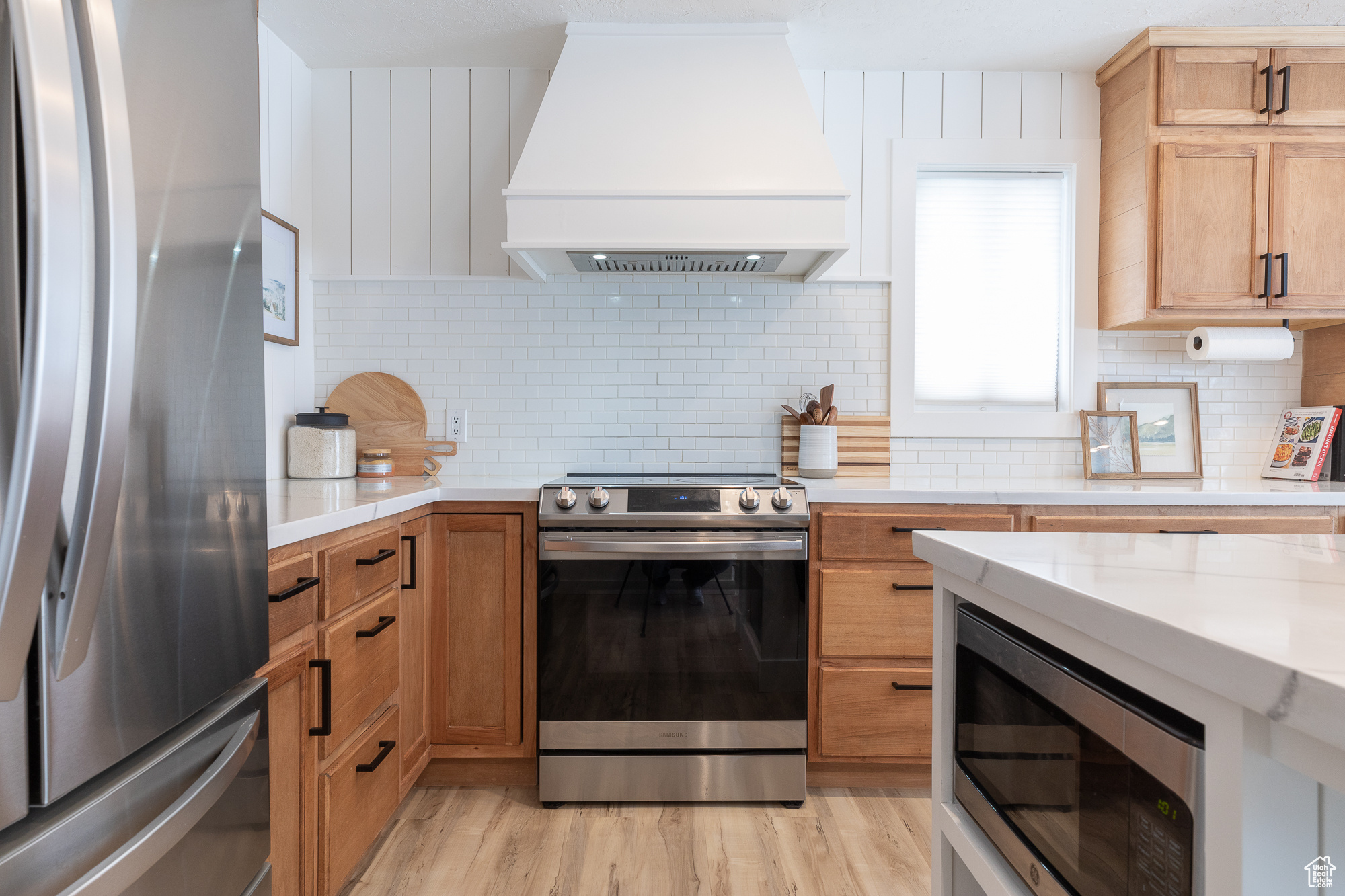 Kitchen with stainless steel appliances, premium range hood, light wood-style floors, and decorative backsplash