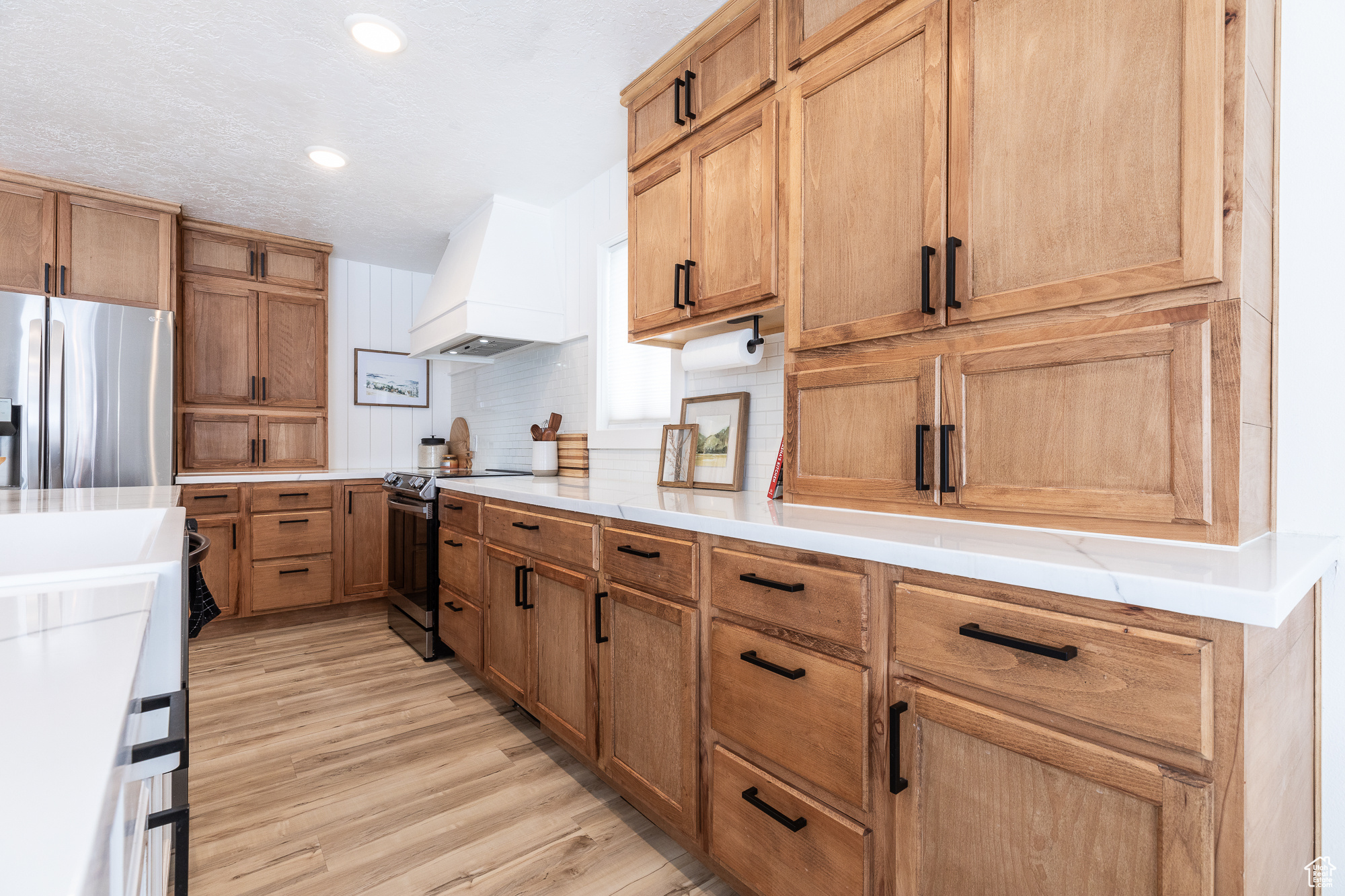 Kitchen with tasteful backsplash, custom range hood, stainless steel appliances, light countertops, and light wood-style floors