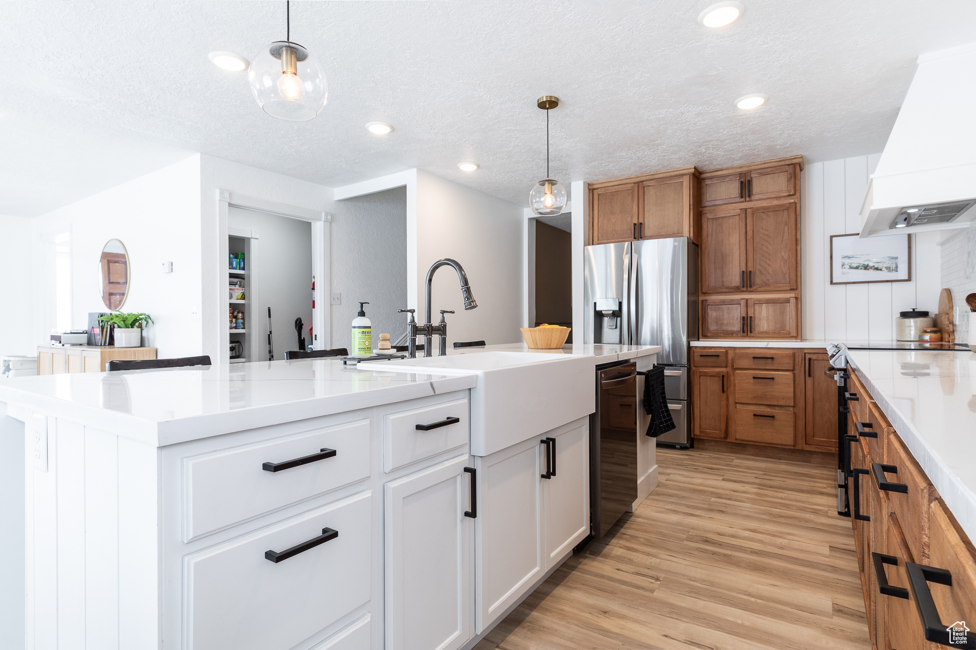 Kitchen with a sink, white cabinets, hanging light fixtures, a large island with sink, and custom range hood