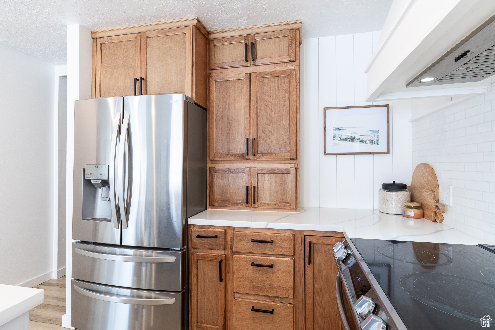 Kitchen with brown cabinets, stainless steel appliances, custom range hood, backsplash, and light wood-style flooring