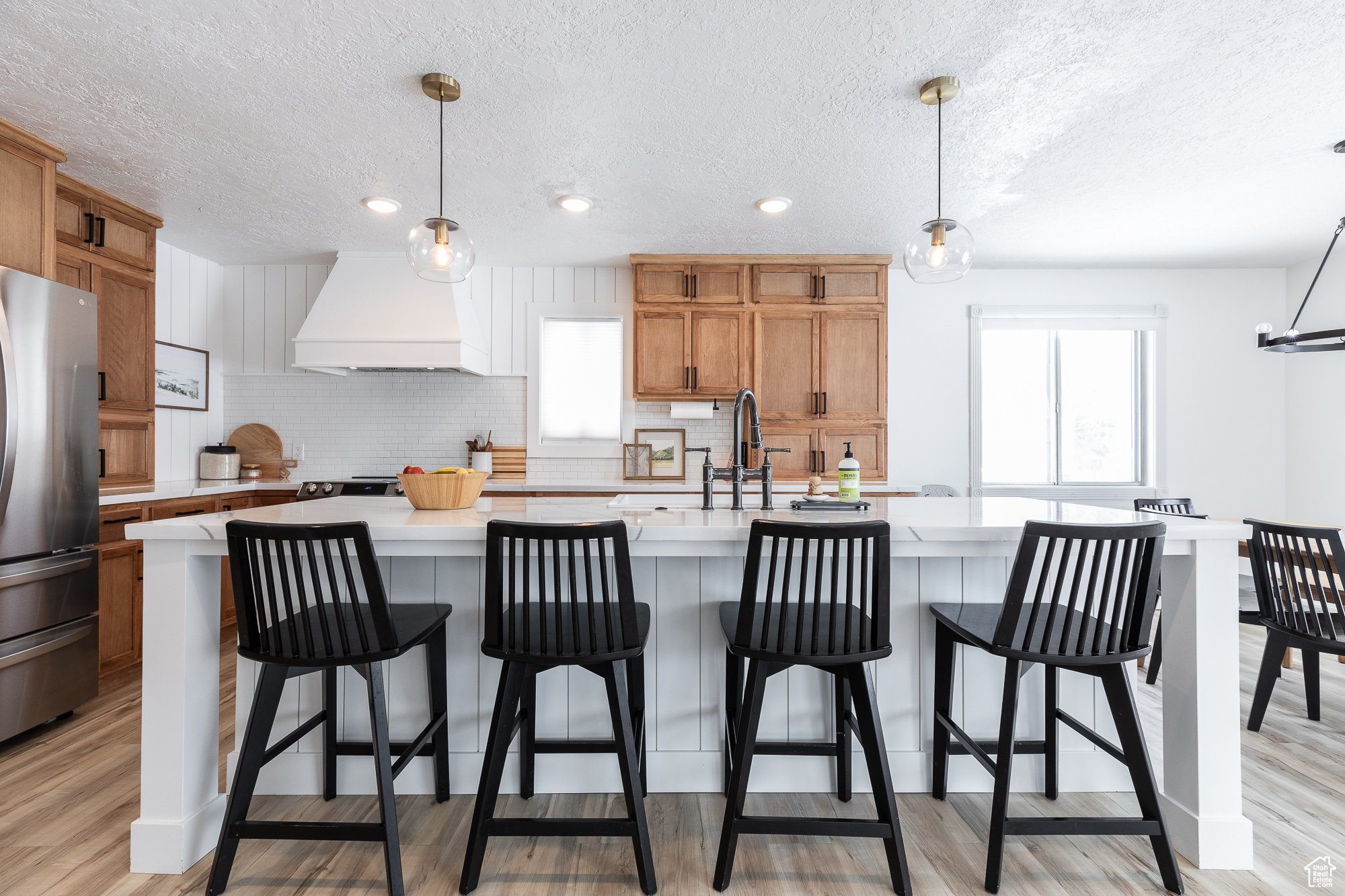Kitchen with light countertops, premium range hood, hanging light fixtures, and freestanding refrigerator