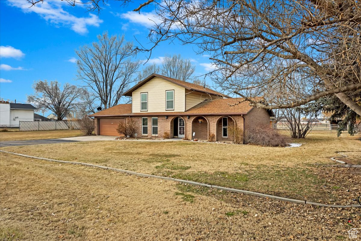 View of front of property featuring an attached garage, brick siding, fence, driveway, and a front yard