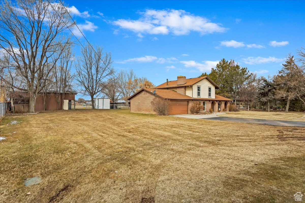 View of property exterior featuring a chimney, a lawn, a storage shed, an attached garage, and fence