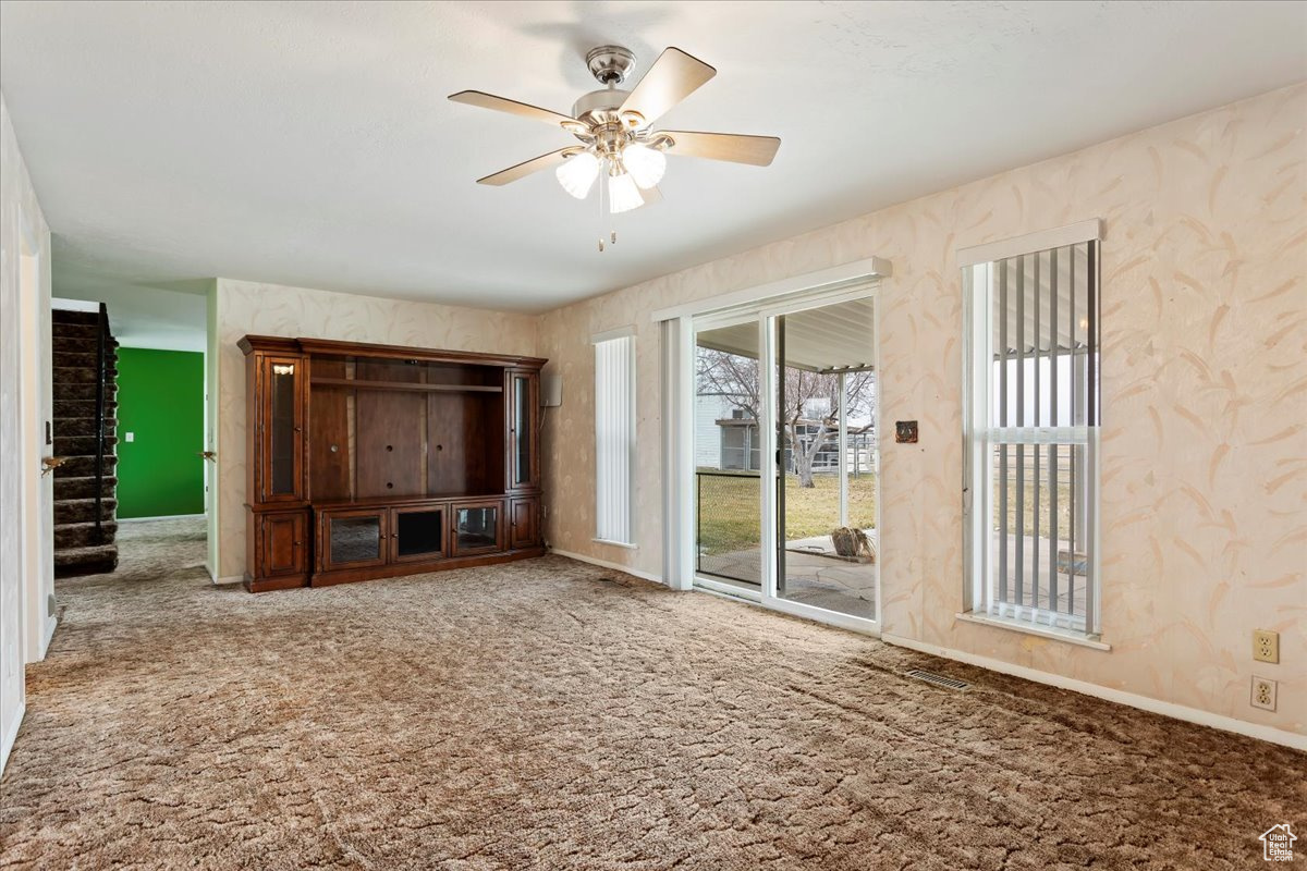 Unfurnished living room featuring wallpapered walls, baseboards, ceiling fan, stairway, and carpet floors