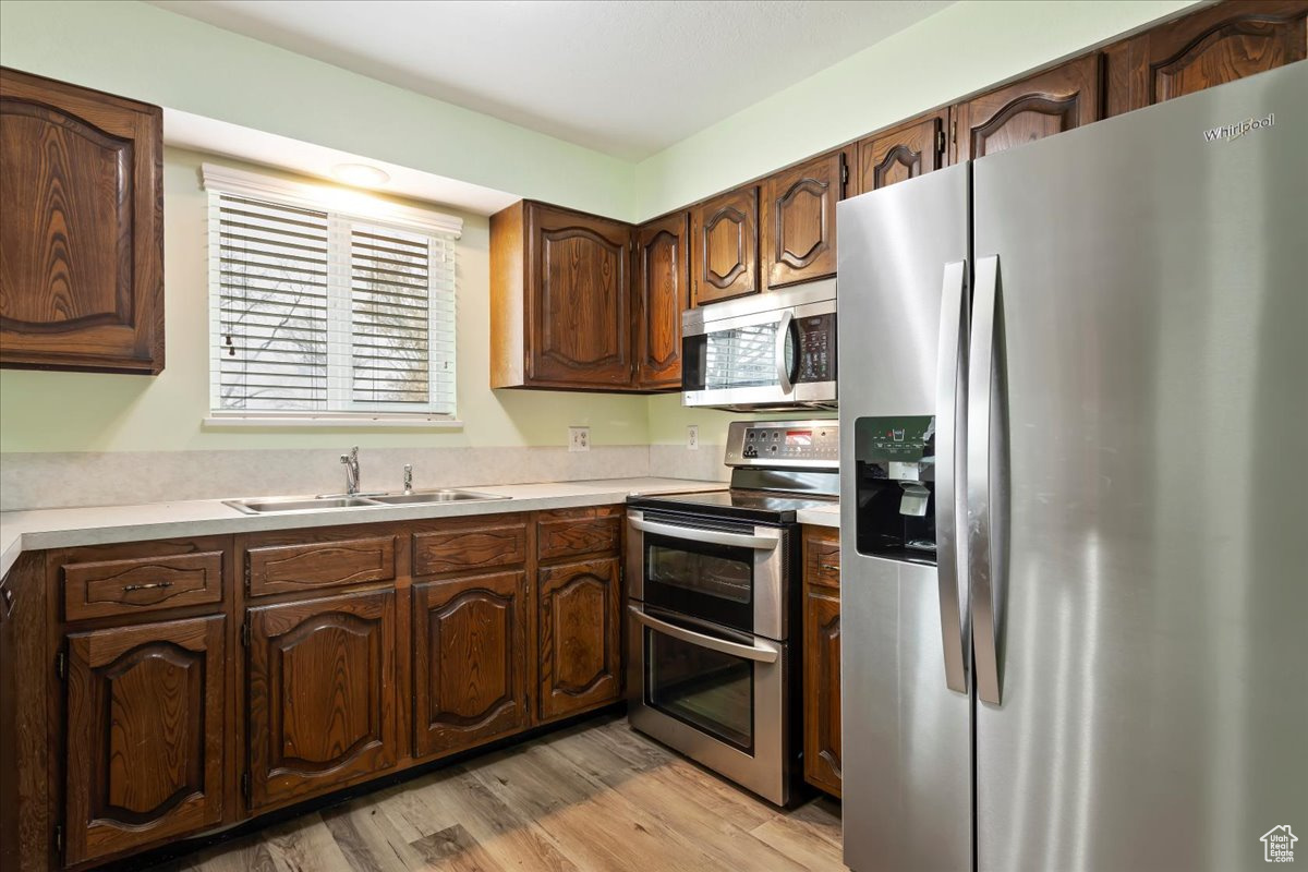 Kitchen featuring stainless steel appliances, light wood-type flooring, a sink, and light countertops
