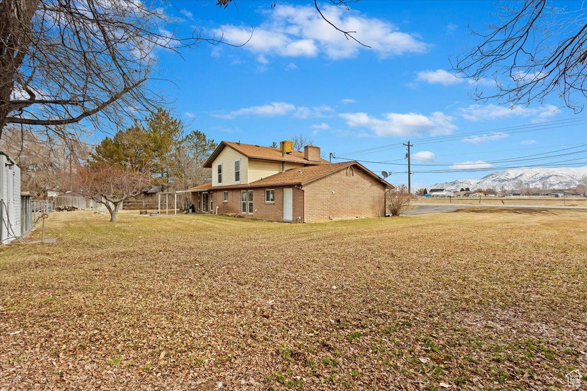 View of side of home with a yard, brick siding, a mountain view, and a chimney