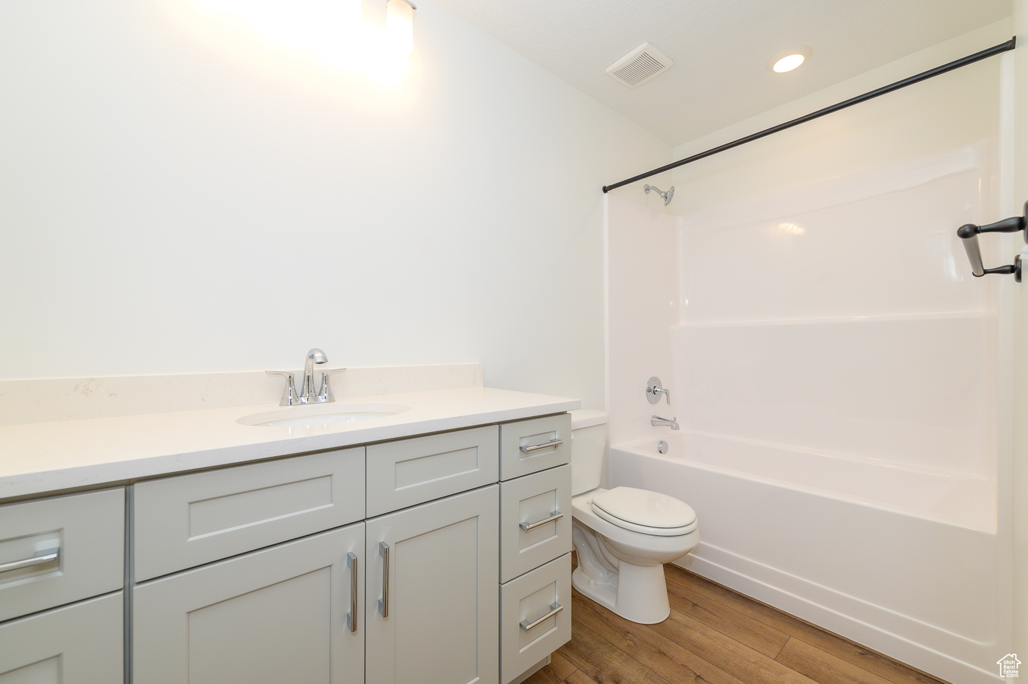 Full bath featuring visible vents, toilet, vanity, wood finished floors, and shower / bathtub combination
