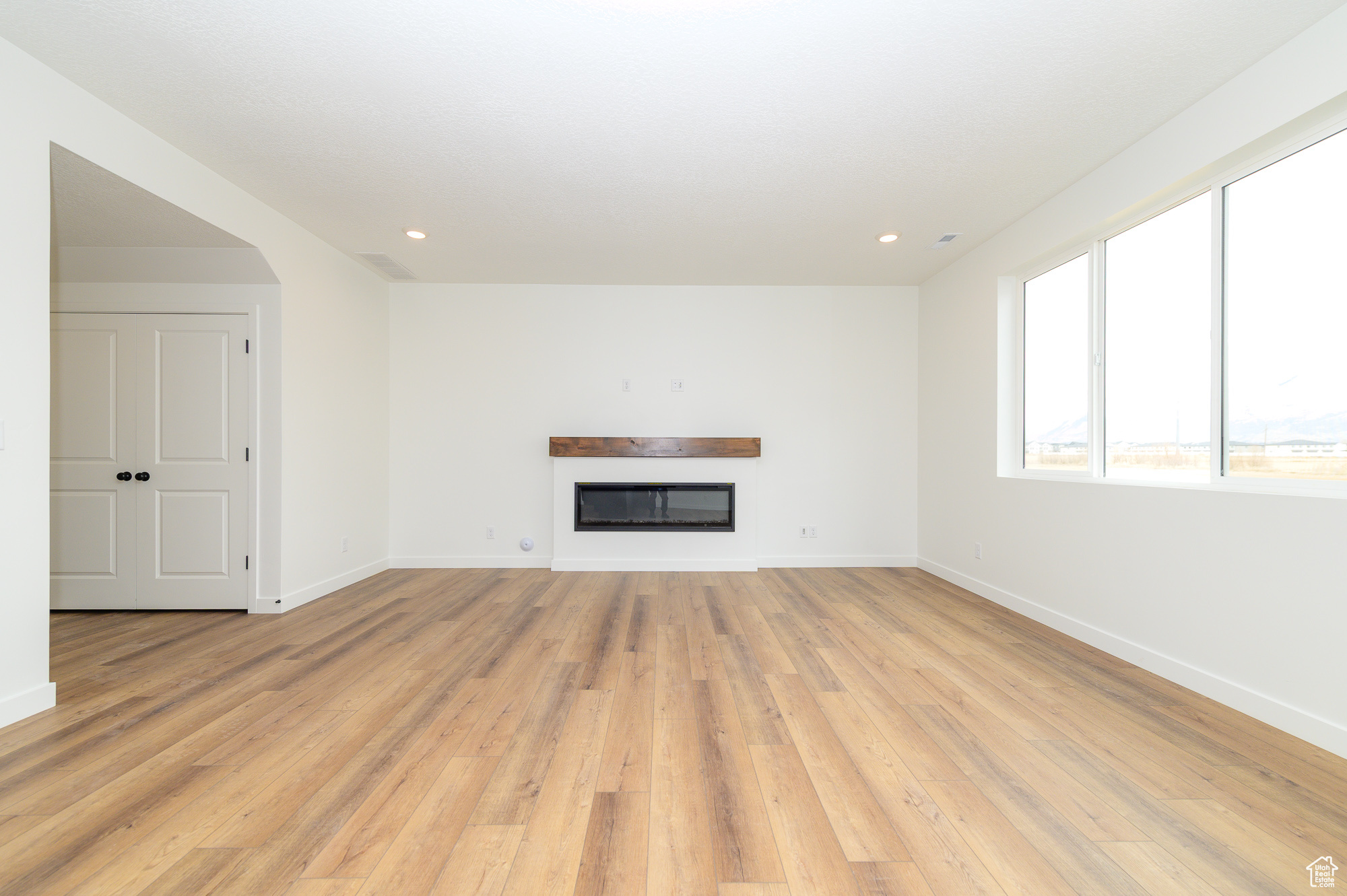 Unfurnished living room featuring light wood finished floors, recessed lighting, baseboards, and a glass covered fireplace
