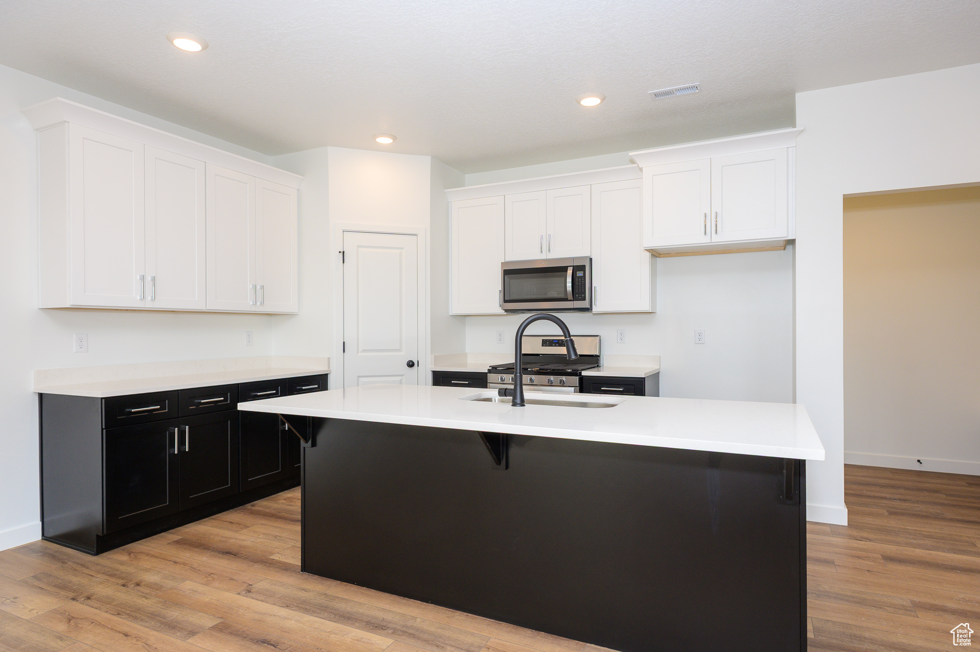 Kitchen featuring appliances with stainless steel finishes, light countertops, white cabinets, and a kitchen island with sink