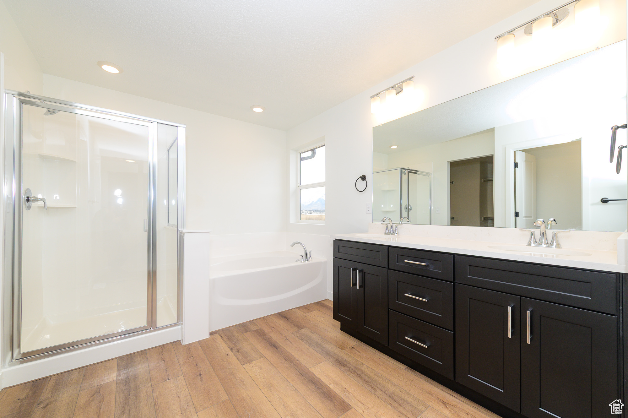 Full bath featuring double vanity, wood finished floors, a garden tub, a shower stall, and a sink