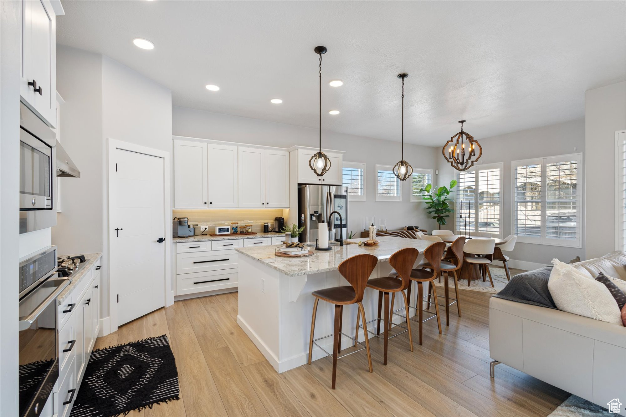 Kitchen with white cabinetry, light stone counters, an island with sink, and hanging light fixtures