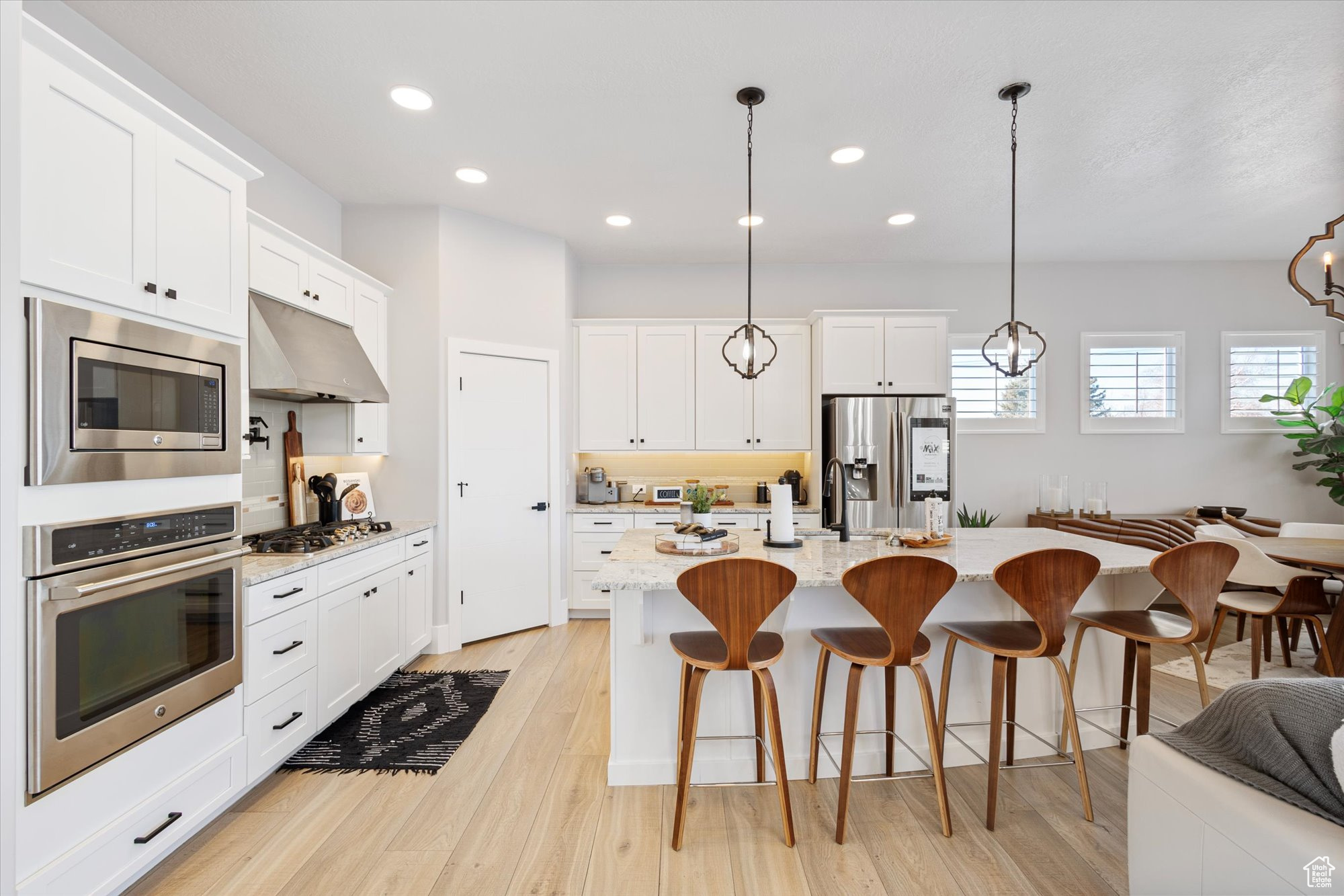 Kitchen with light stone counters, white cabinetry, decorative light fixtures, a center island with sink, and appliances with stainless steel finishes