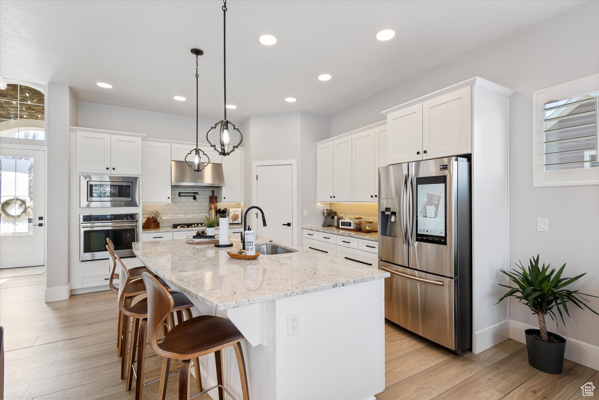 Kitchen featuring white cabinetry, an island with sink, sink, light stone counters, and stainless steel appliances