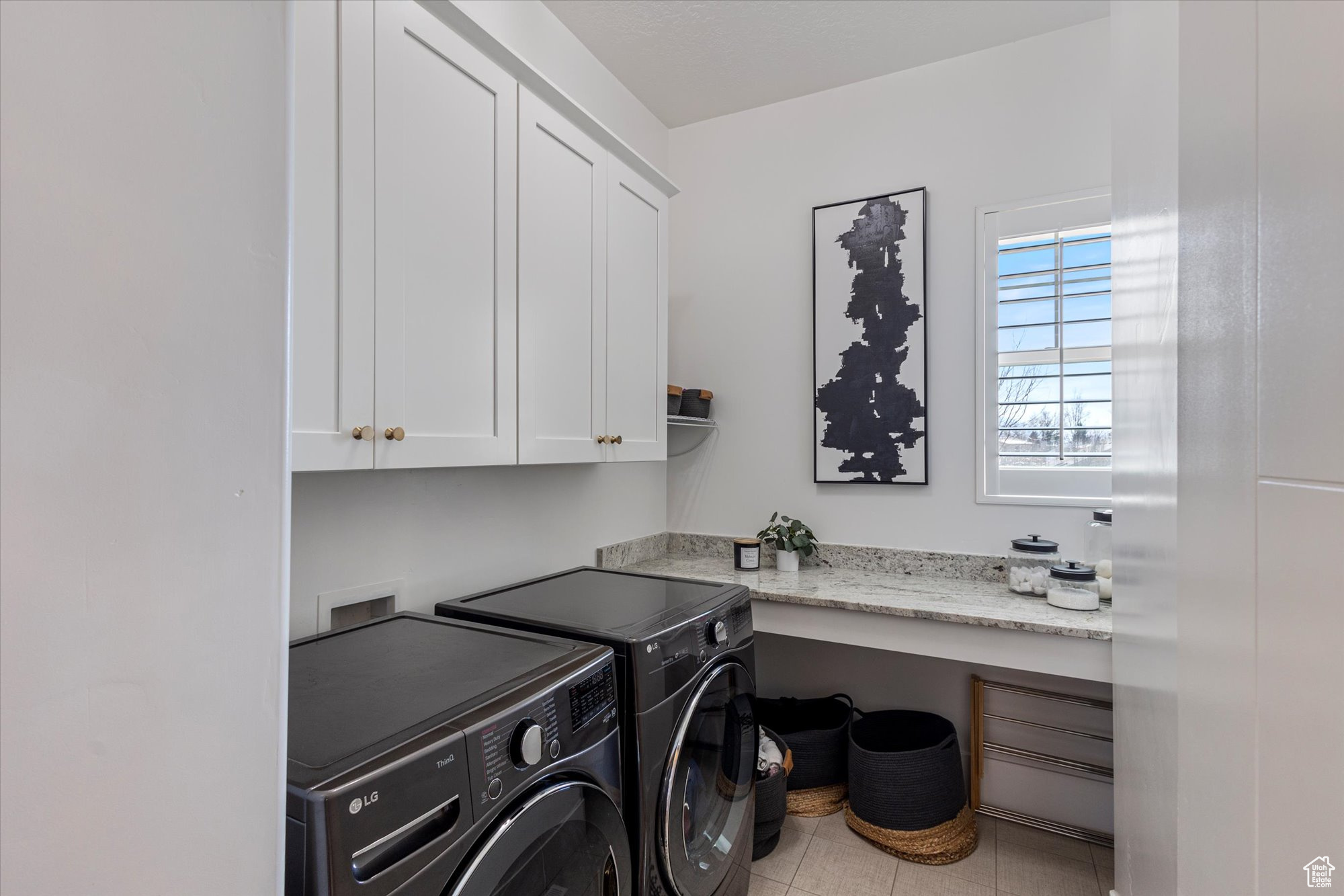Clothes washing area featuring cabinets, washing machine and clothes dryer, and light tile patterned flooring