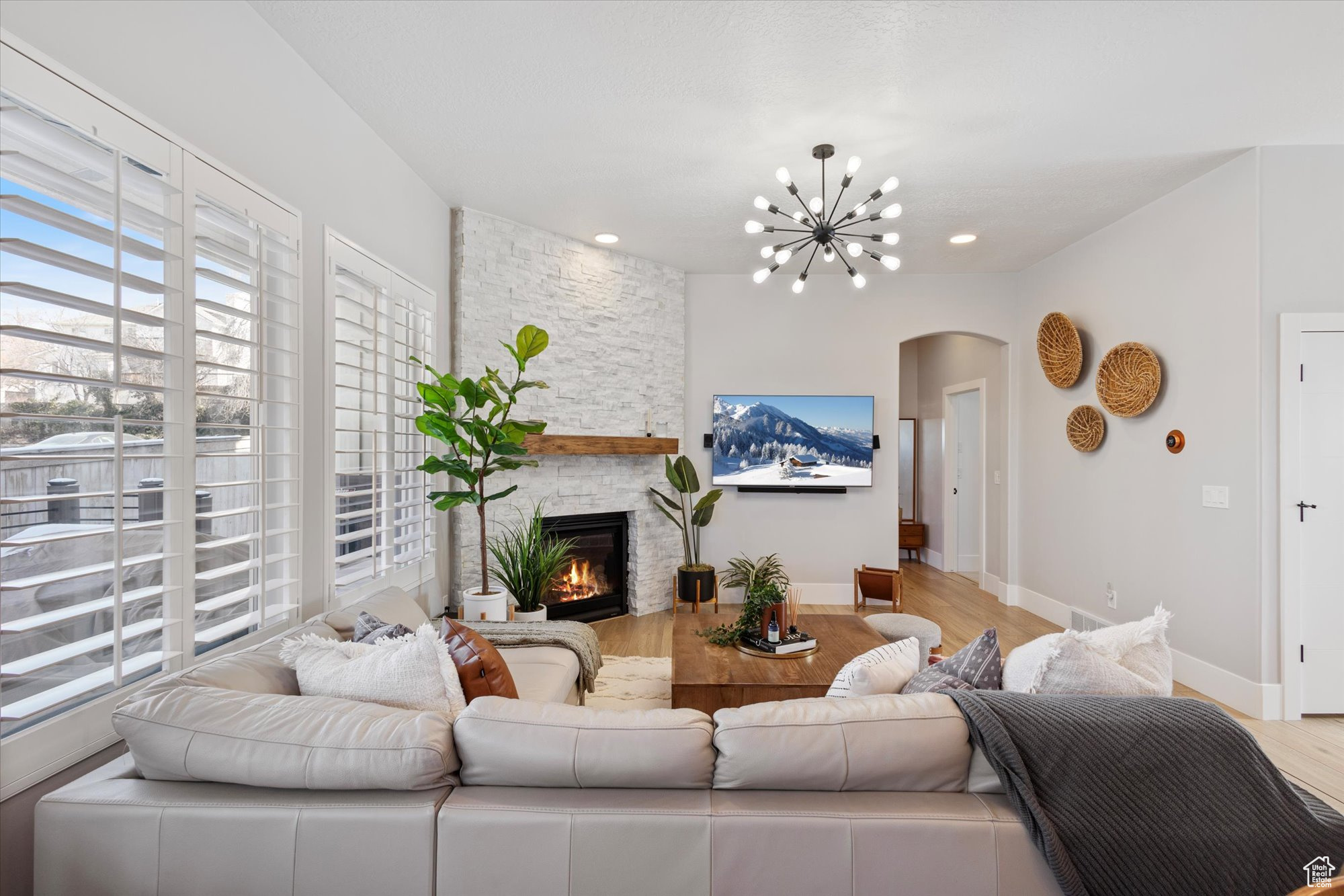 Living room with an inviting chandelier, a stone fireplace, and light wood-type flooring