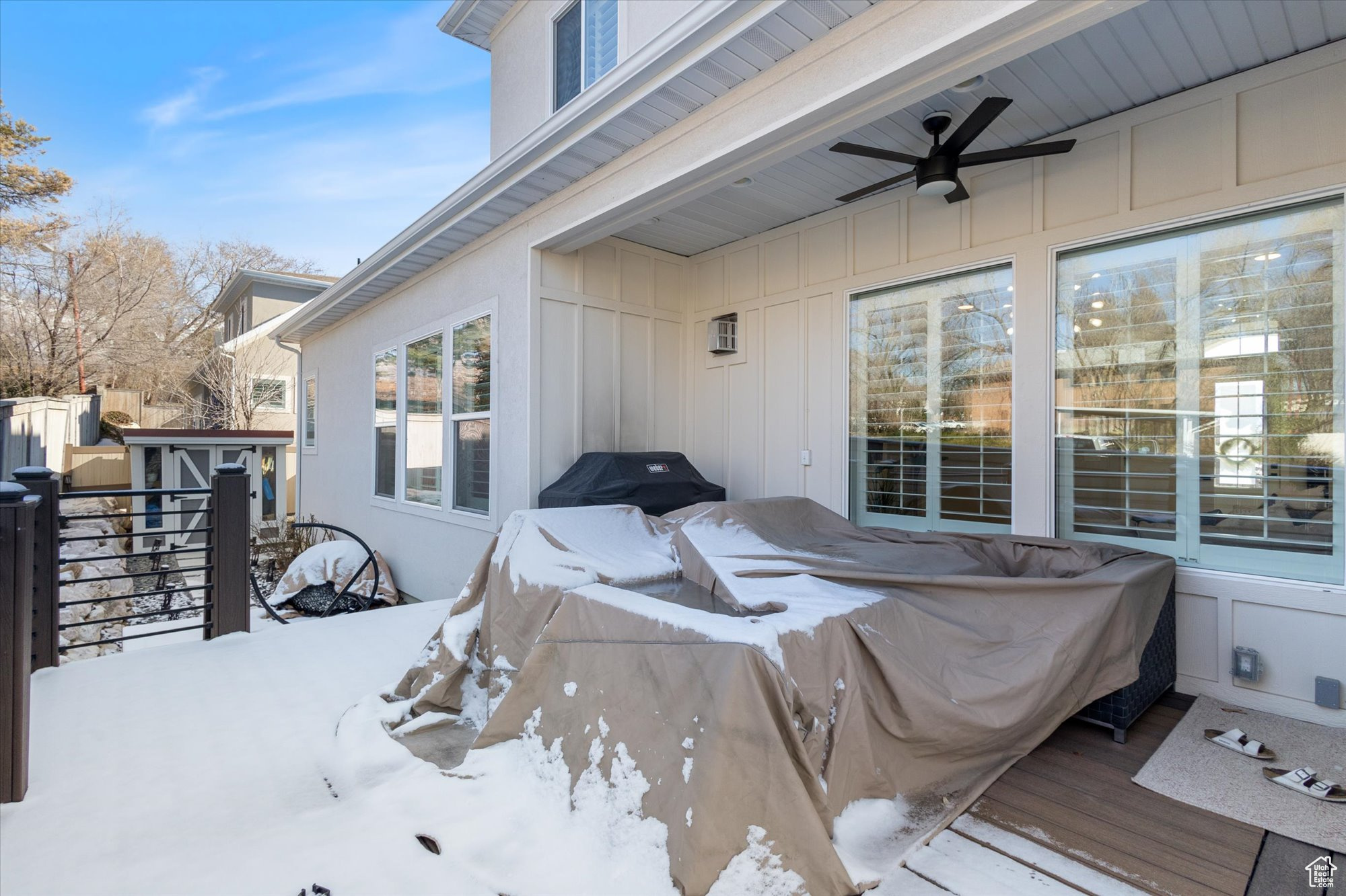 Snow covered patio with a wooden deck, ceiling fan, and a storage shed