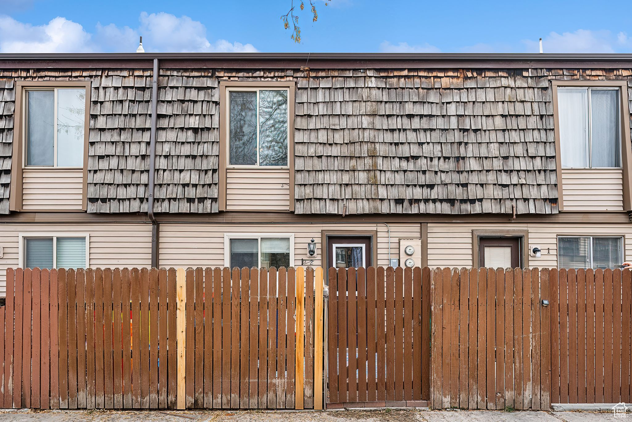 View of side of property featuring fence and mansard roof