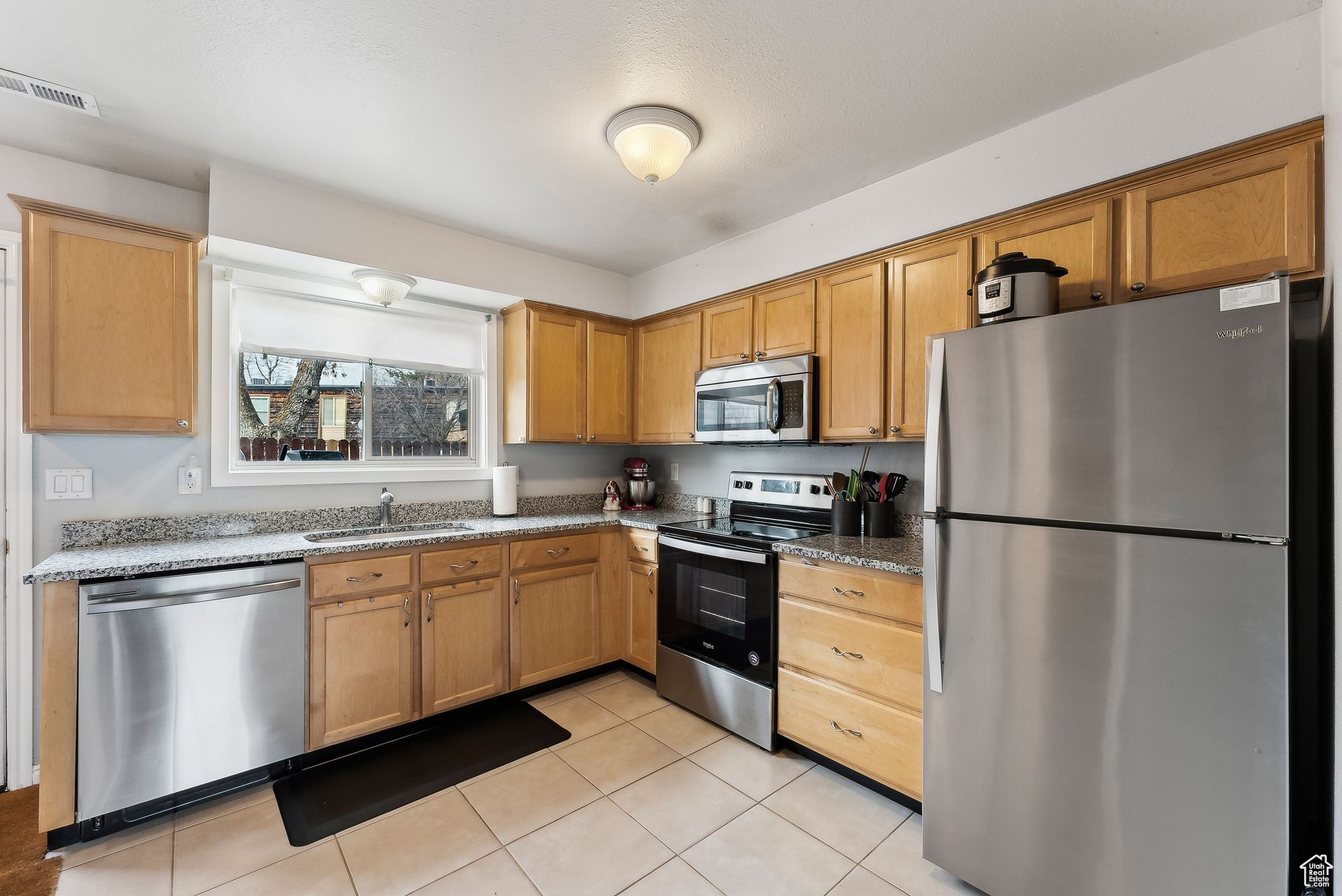 Kitchen featuring light tile patterned floors, visible vents, appliances with stainless steel finishes, stone countertops, and a sink