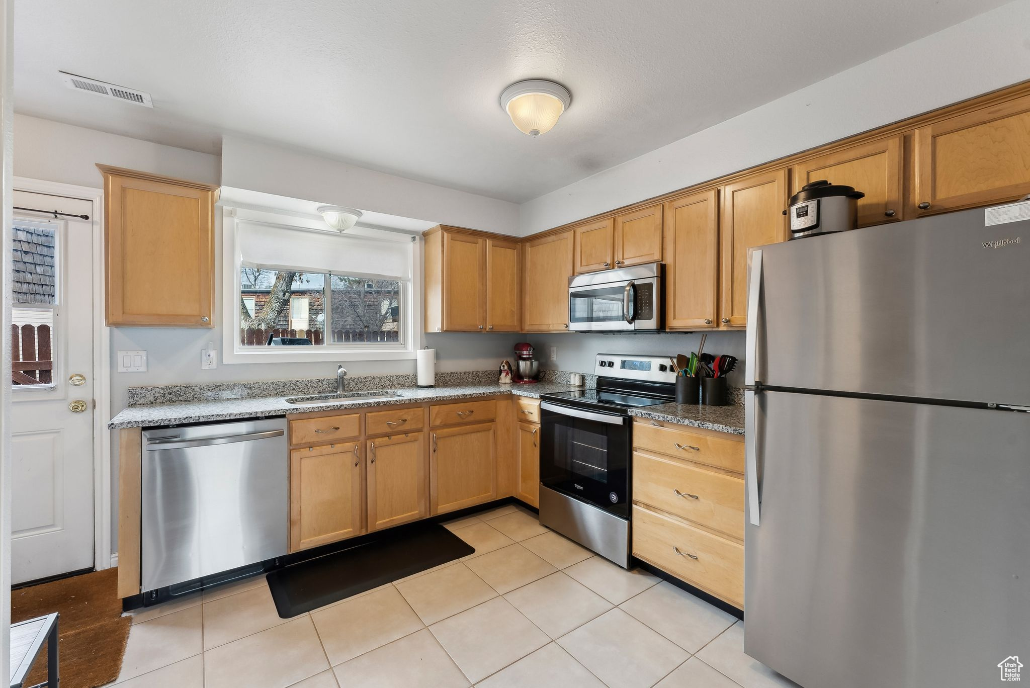 Kitchen with stone counters, light tile patterned flooring, a sink, visible vents, and appliances with stainless steel finishes