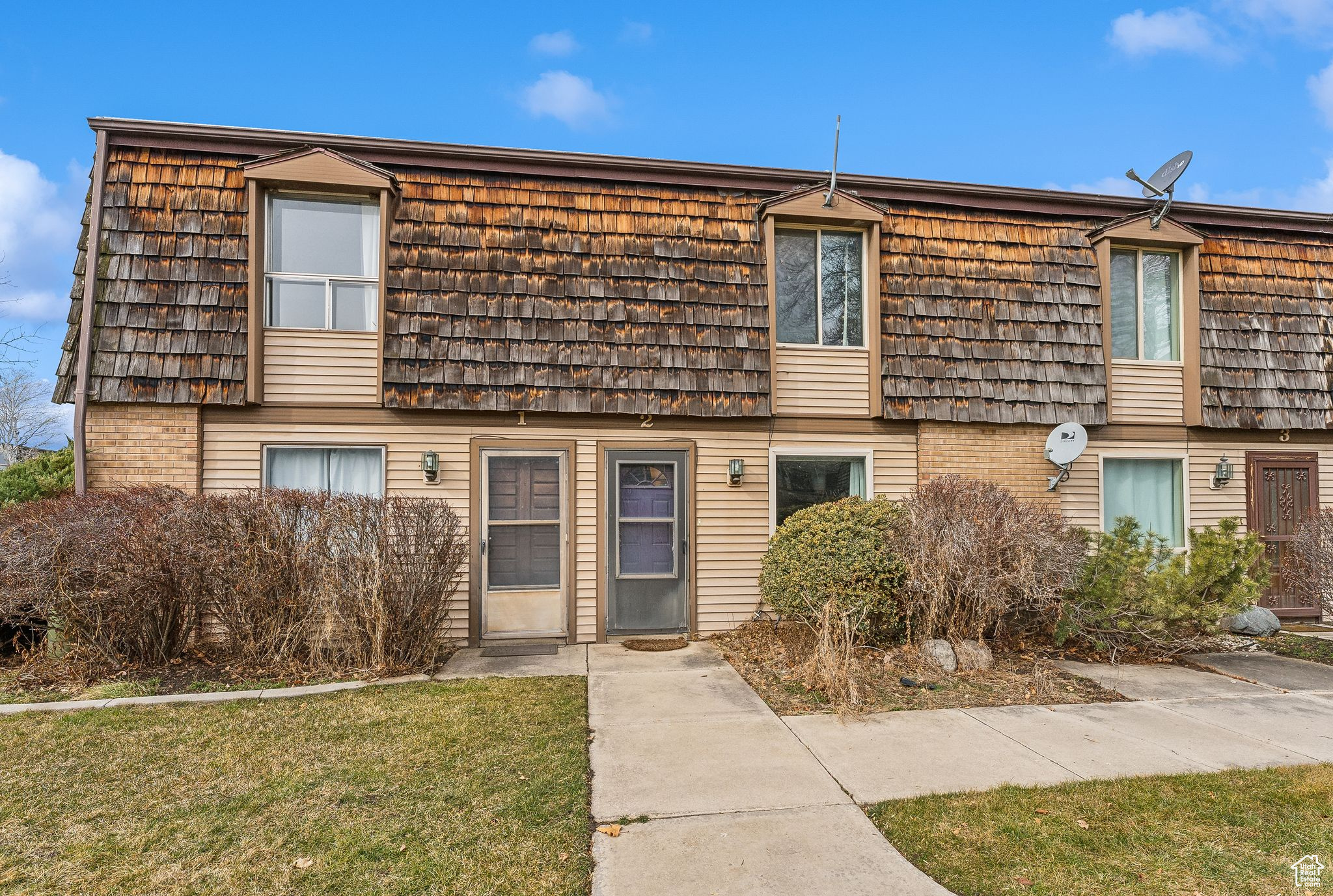 Townhome / multi-family property featuring brick siding, a front lawn, and mansard roof