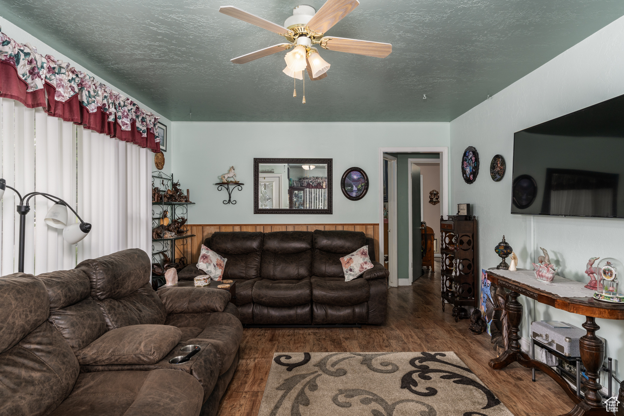 Living room featuring a textured ceiling, wainscoting, wood finished floors, and a ceiling fan