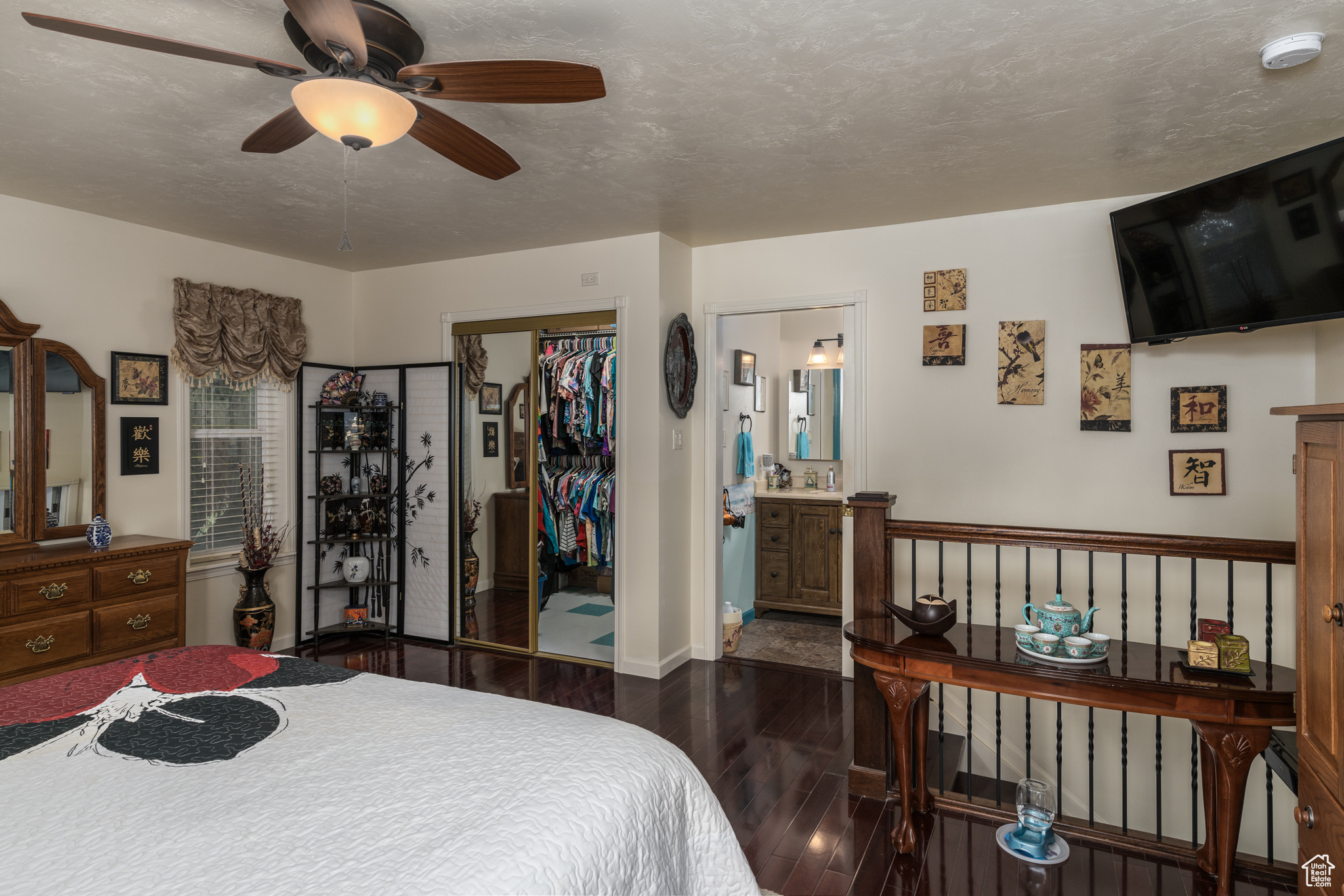 Bedroom featuring a textured ceiling, a ceiling fan, a closet, dark wood-style floors, and ensuite bath