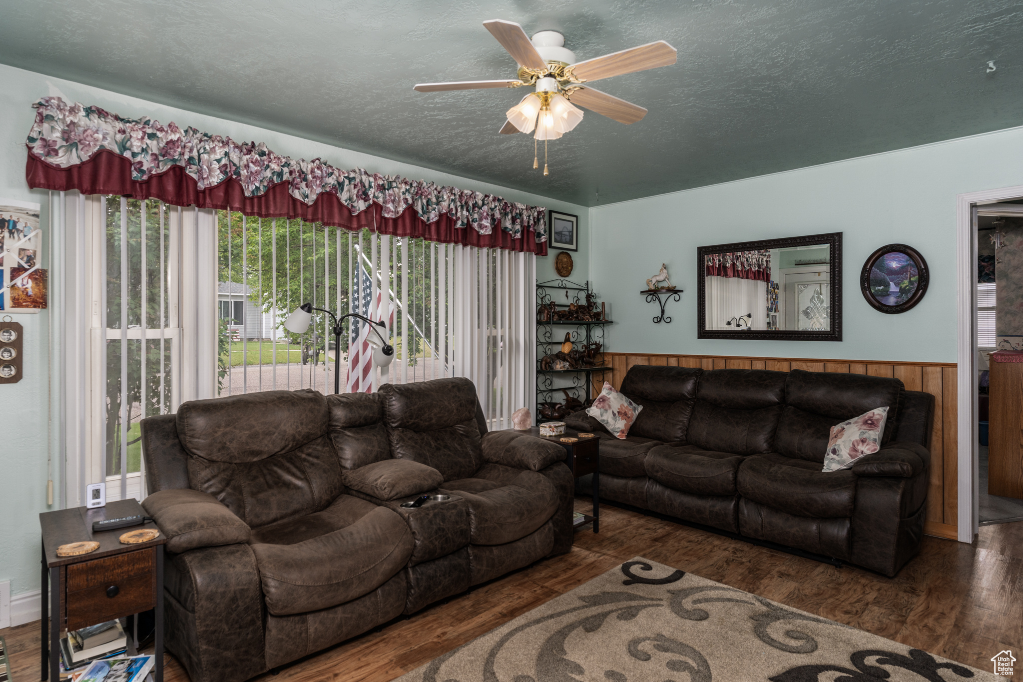 Living room with a ceiling fan, dark wood-style flooring, wainscoting, and a textured ceiling